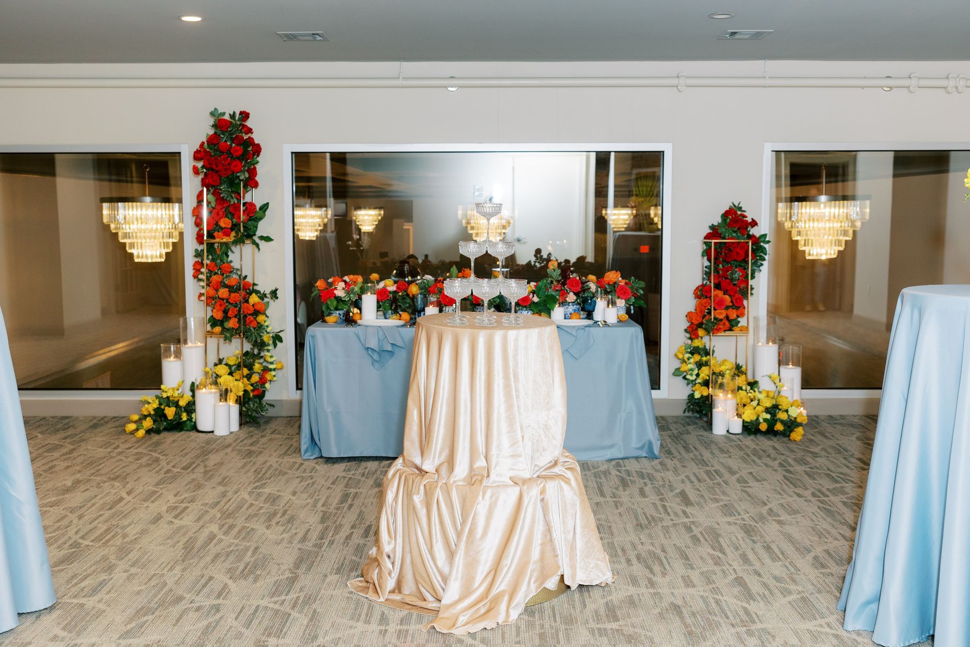 Reception setup: Gold-draped table in front of buffet tables with blue tablecloths, floral arrangements, and candles.