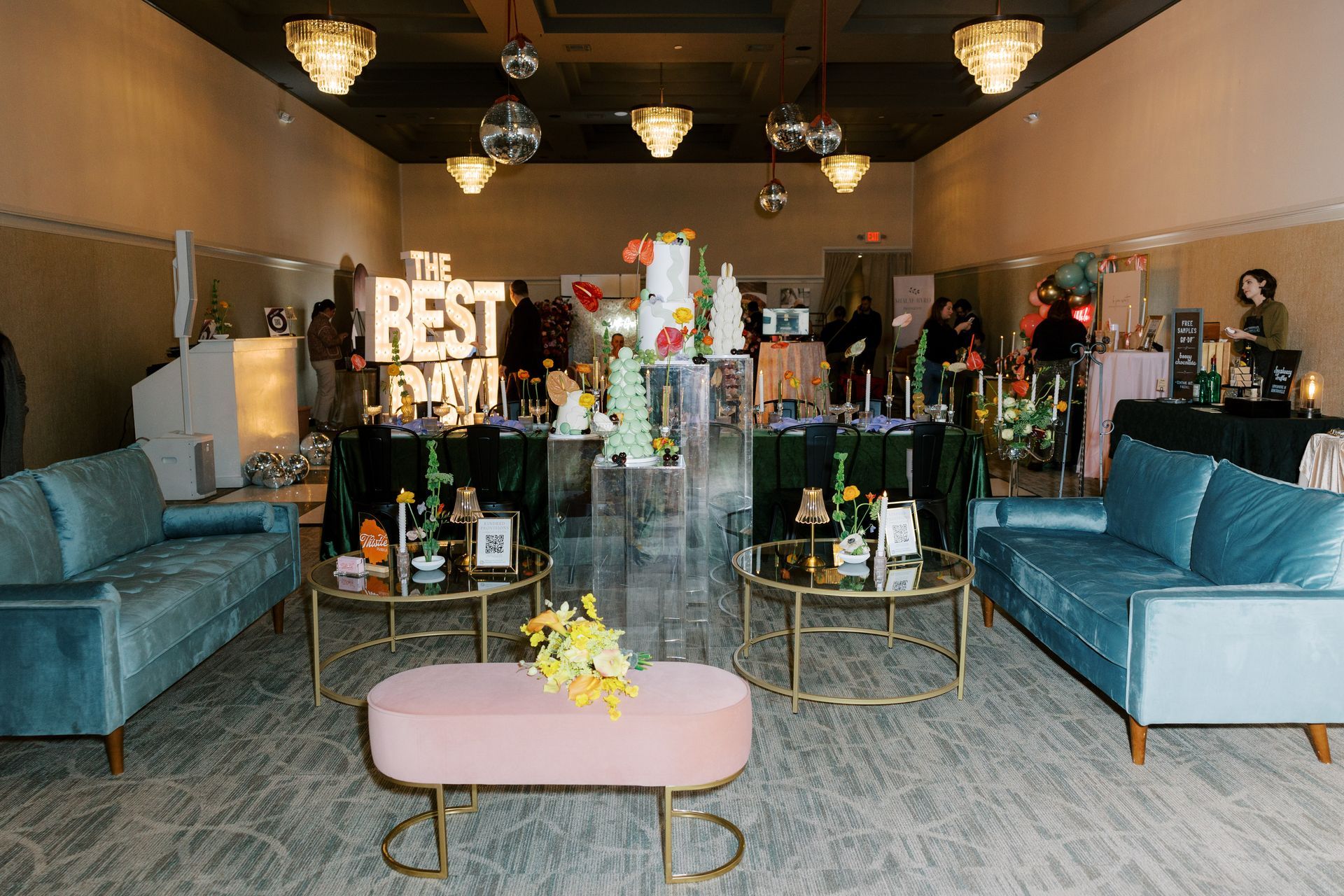 Event space with teal sofas, pink ottoman, tables with decor, cakes, and 