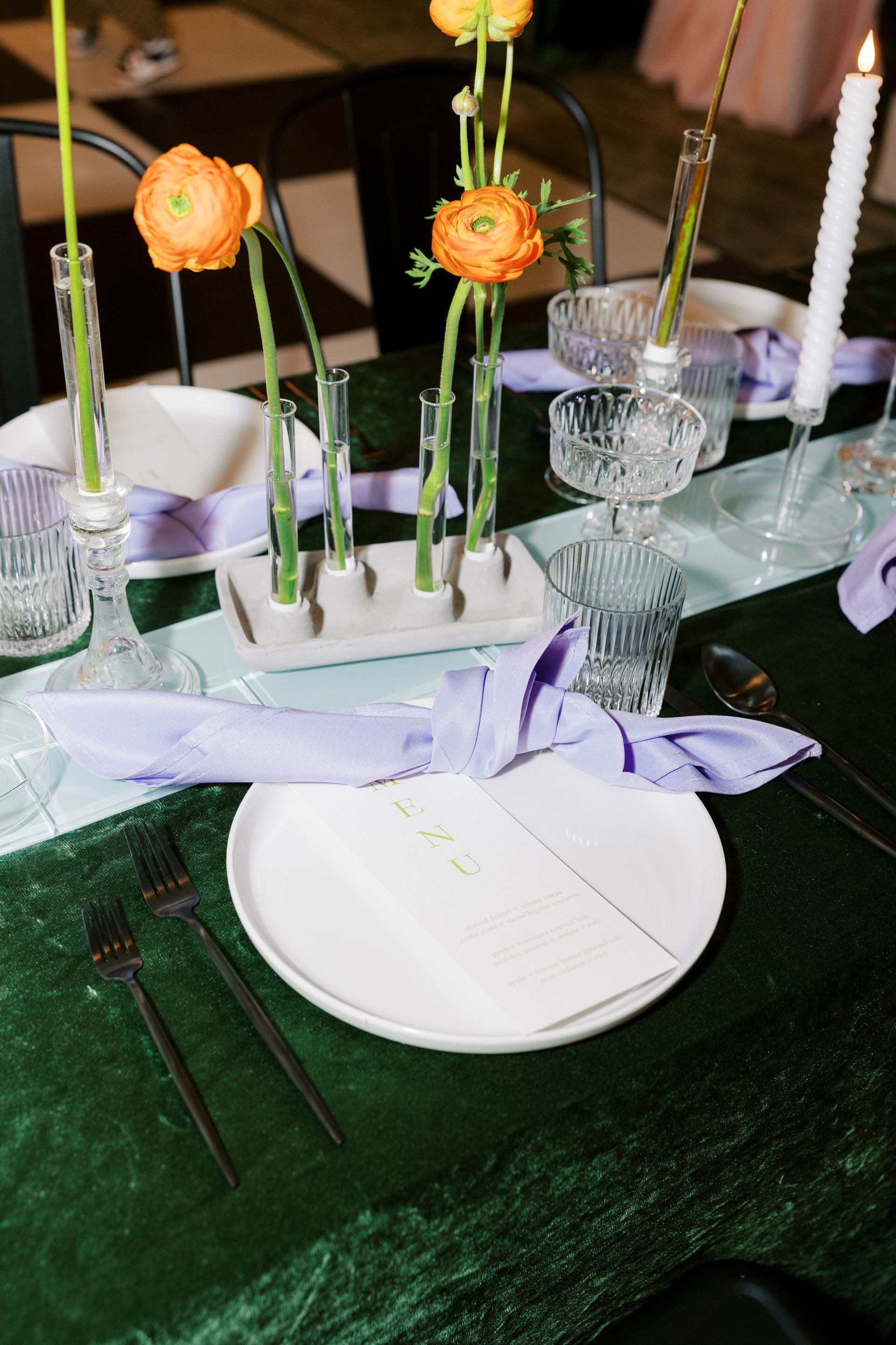 Formal table setting with orange flowers, candles, and purple napkins on a green tablecloth.