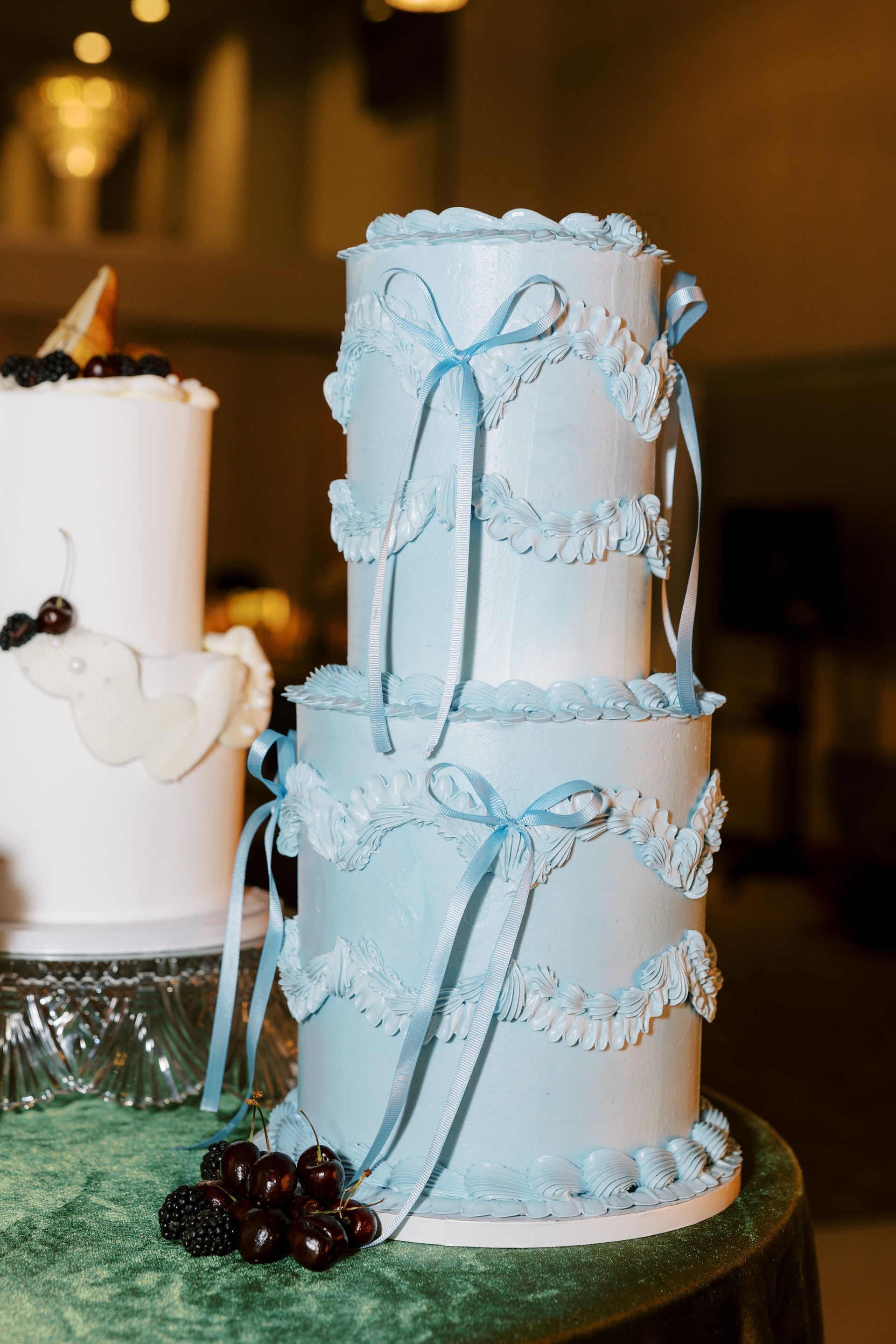 Three-tiered light blue cake, decorated with lace and ribbons, sitting on a round table.