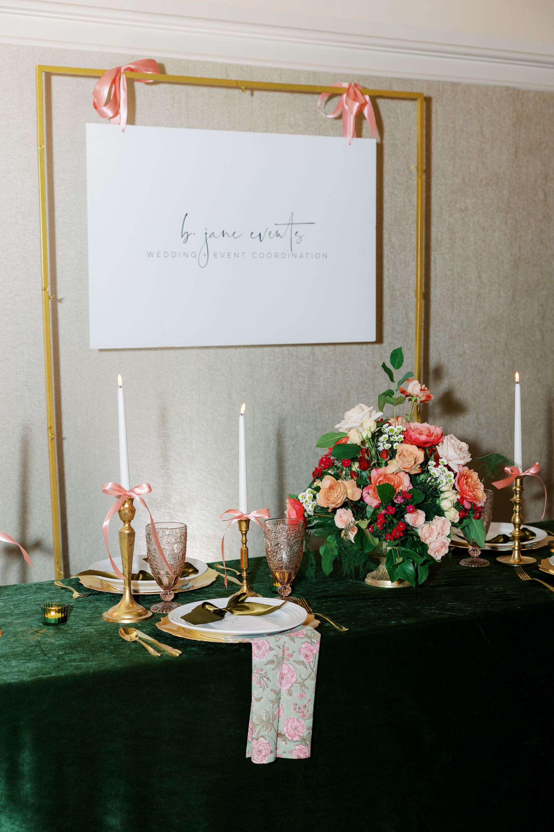 Elegant table setting with floral arrangement, candles, and sign against a green velvet tablecloth.