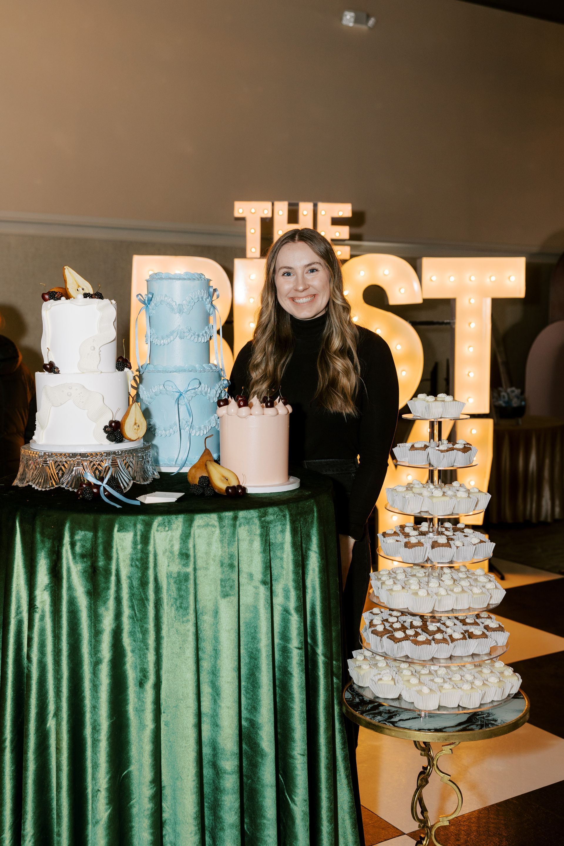 Woman stands behind a table with four decorated cakes under a 