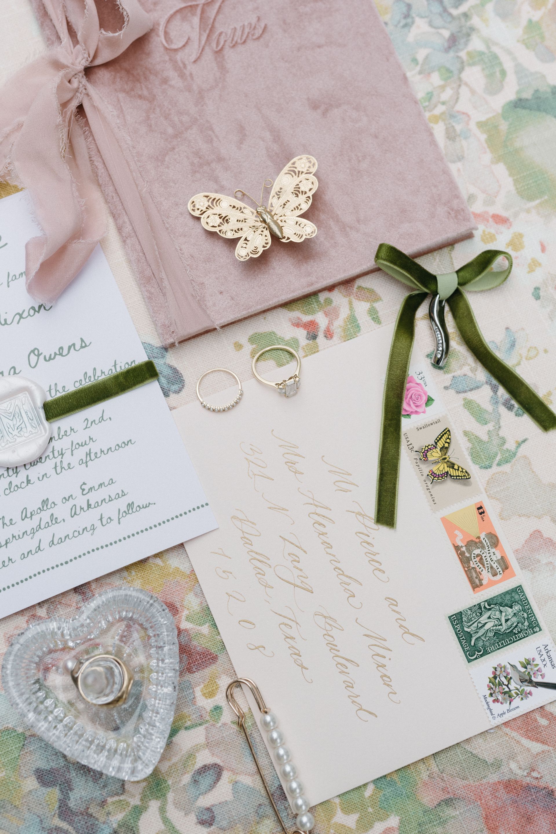 Wedding invitation suite with stationery, rings, and butterfly decorations. Soft pinks, greens, and gold hues.