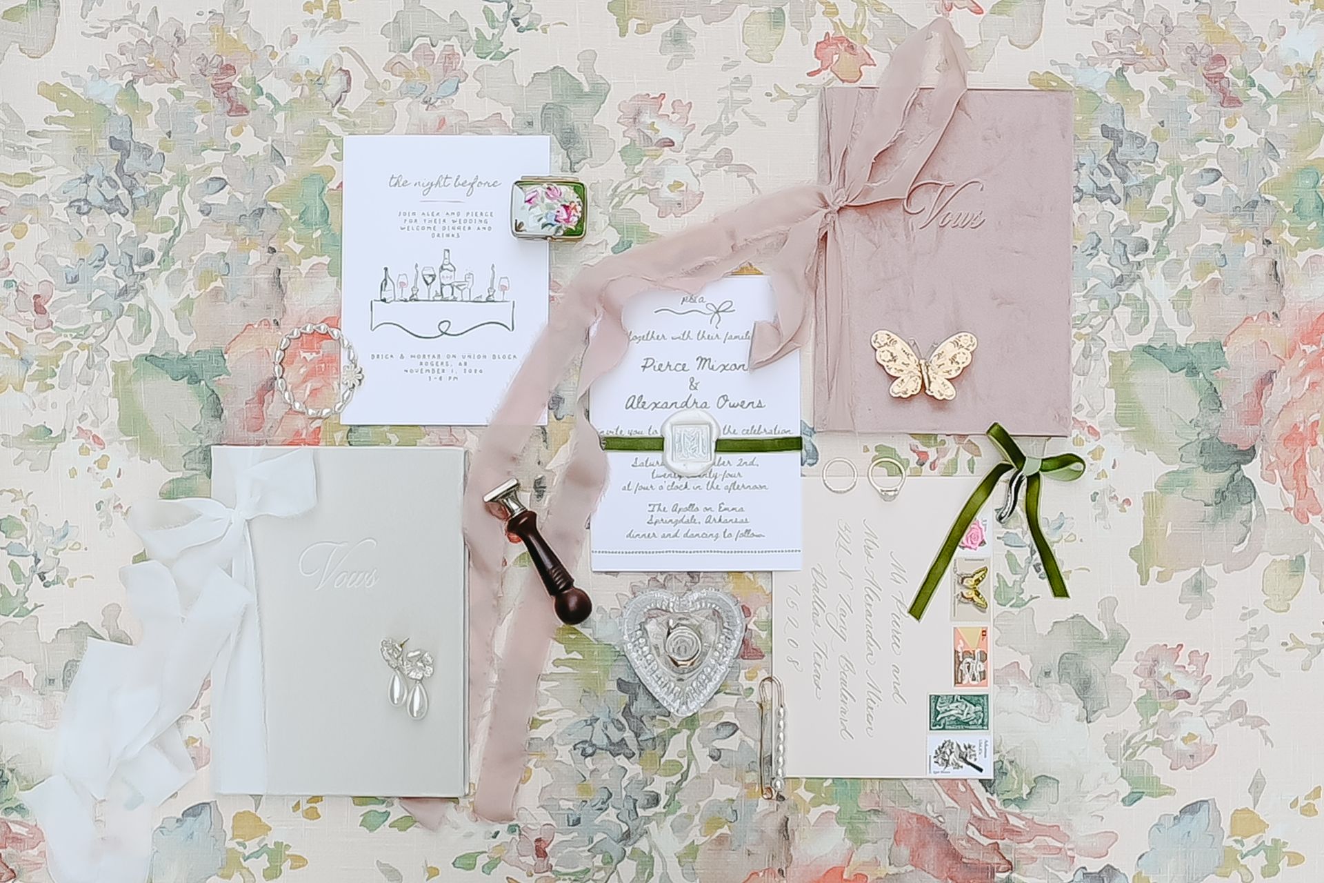 Wedding invitation suite with pink, green, and gold accents on floral background.