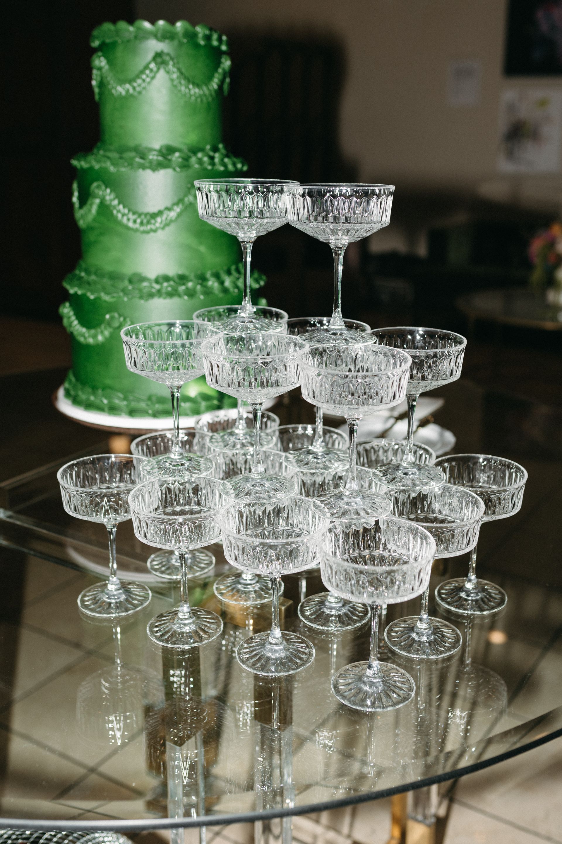 Green tiered cake and champagne glass pyramid on a glass table.