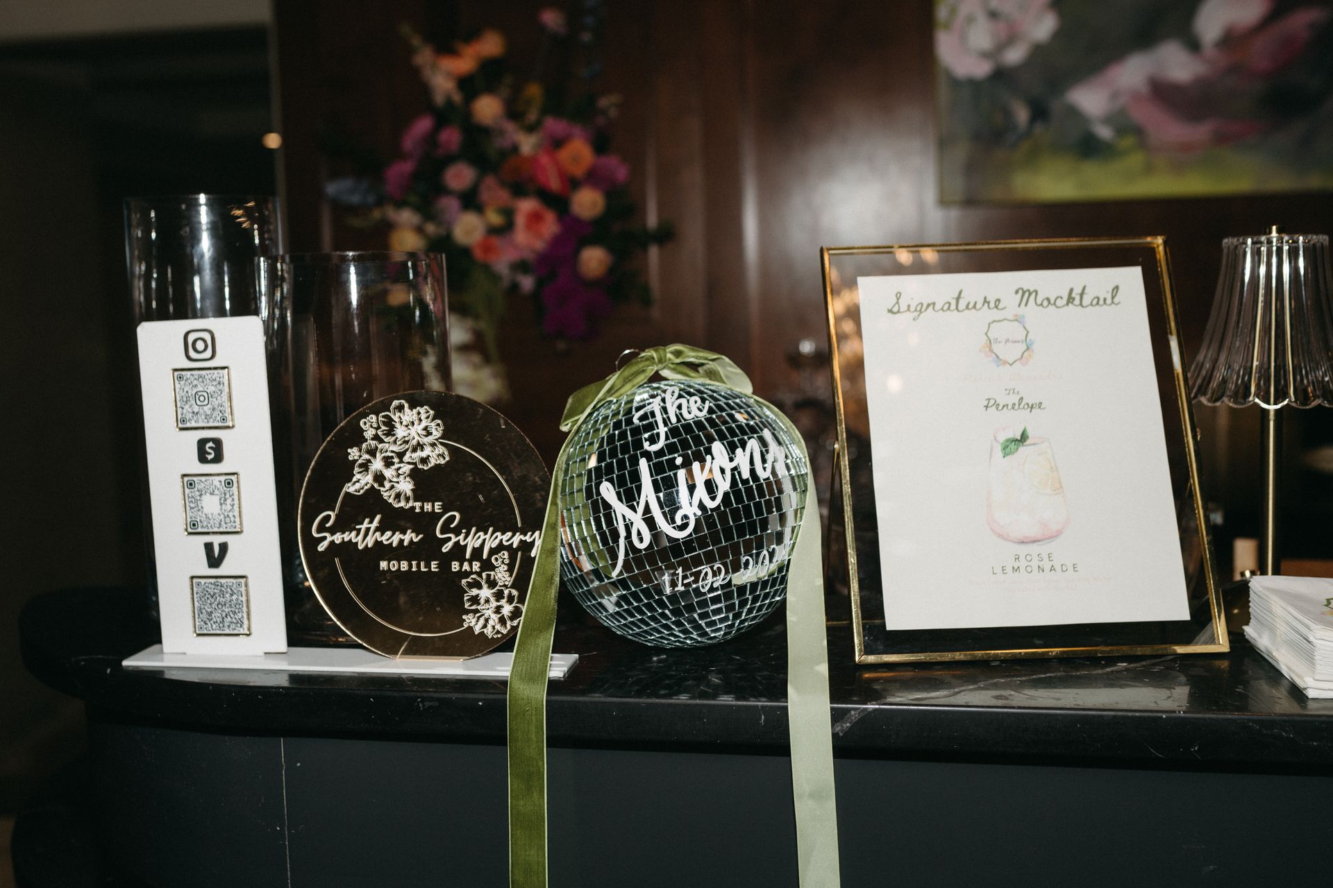 Bar setup with drink menu, florals, decorative objects, and QR code on a black surface.