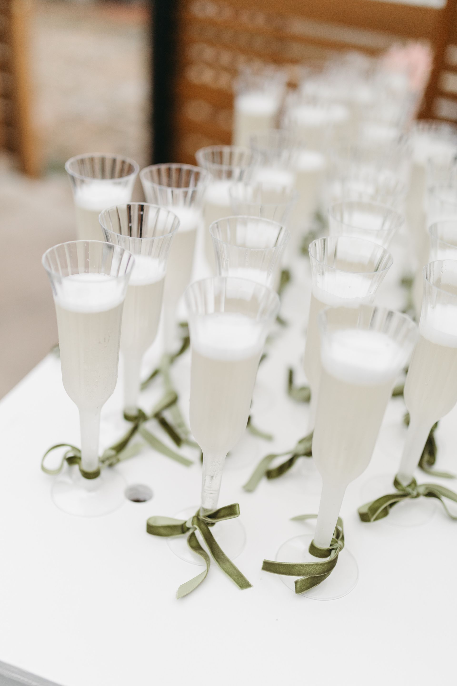 Champagne flutes filled with bubbly drink, tied with green ribbon, lined on a white table.