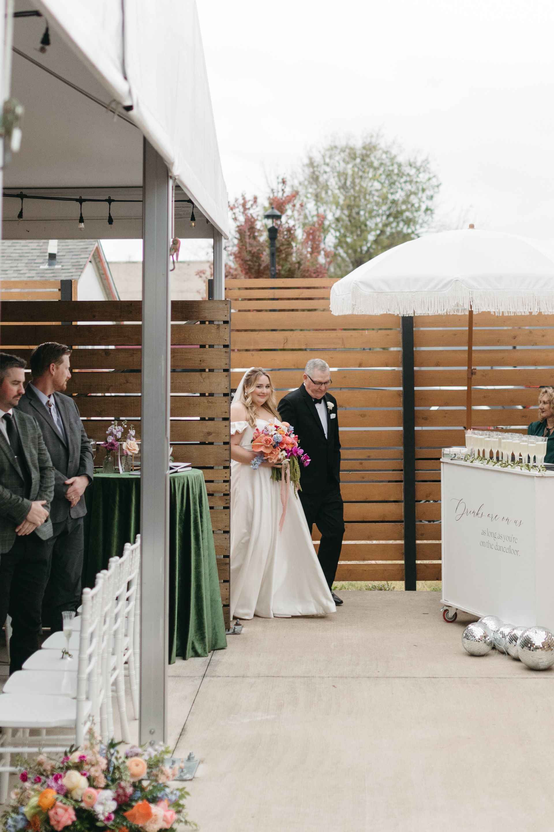 Bride walks down aisle with her father at an outdoor wedding.