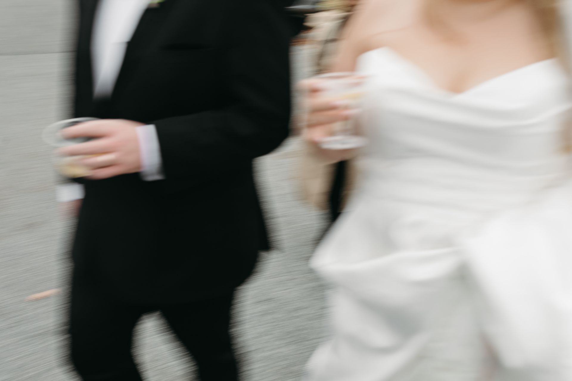 Blurred photo of a couple, man in a suit, woman in a white wedding dress, both holding drinks.
