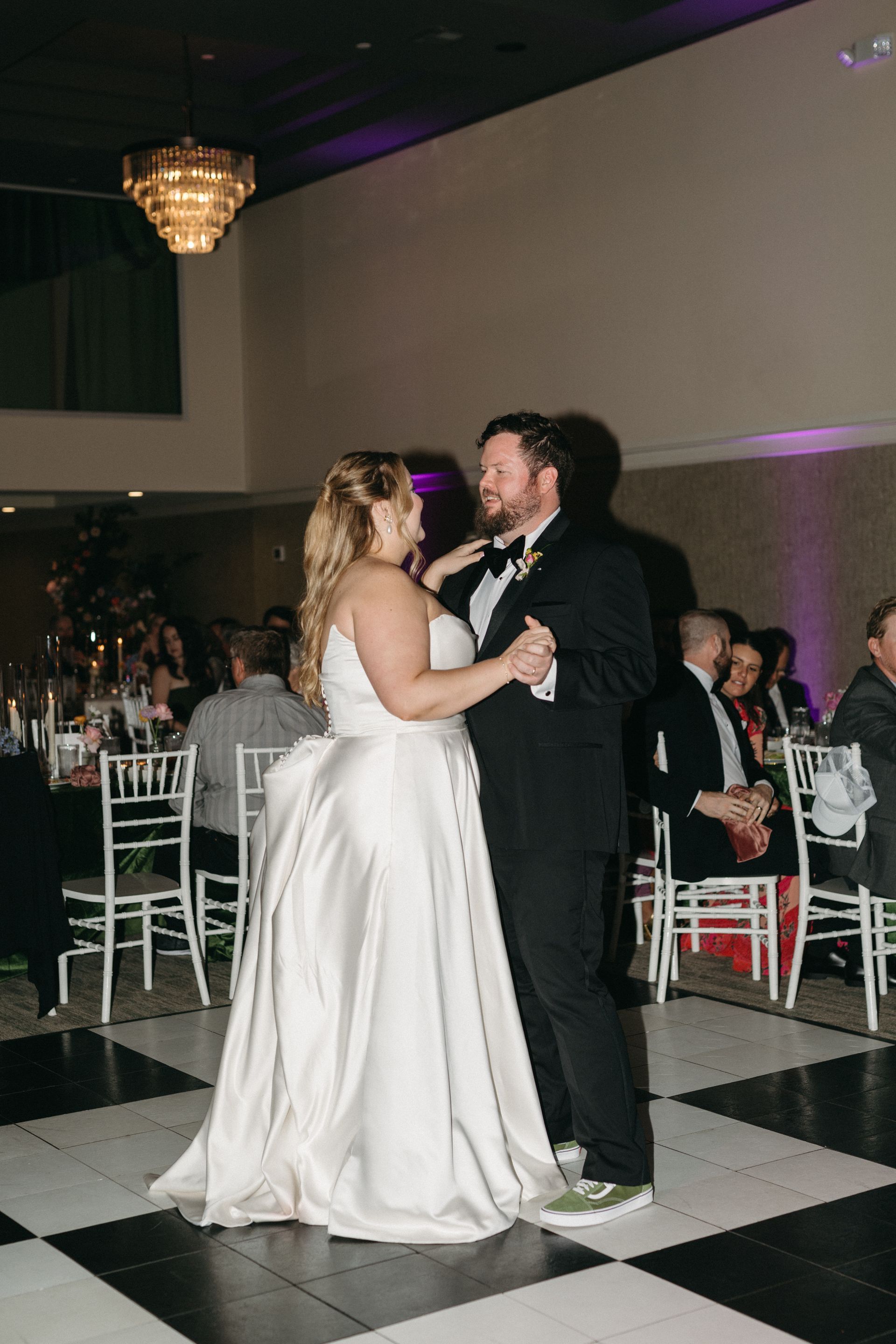 Bride and groom dance at reception. Bride in white gown, groom in tuxedo. Black and white checkered dance floor.