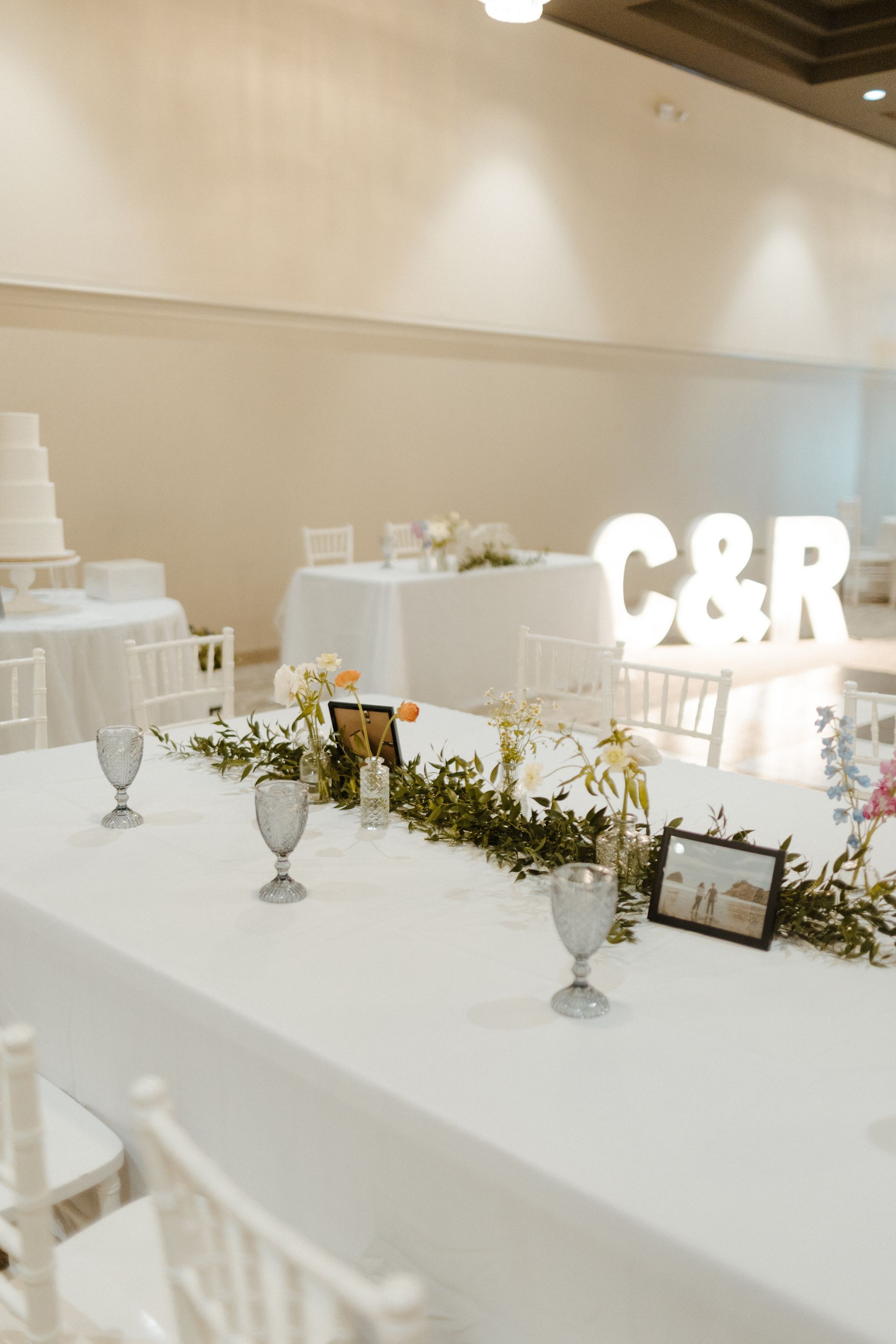 Wedding reception table set with flowers, candles, and cake in a brightly lit room.