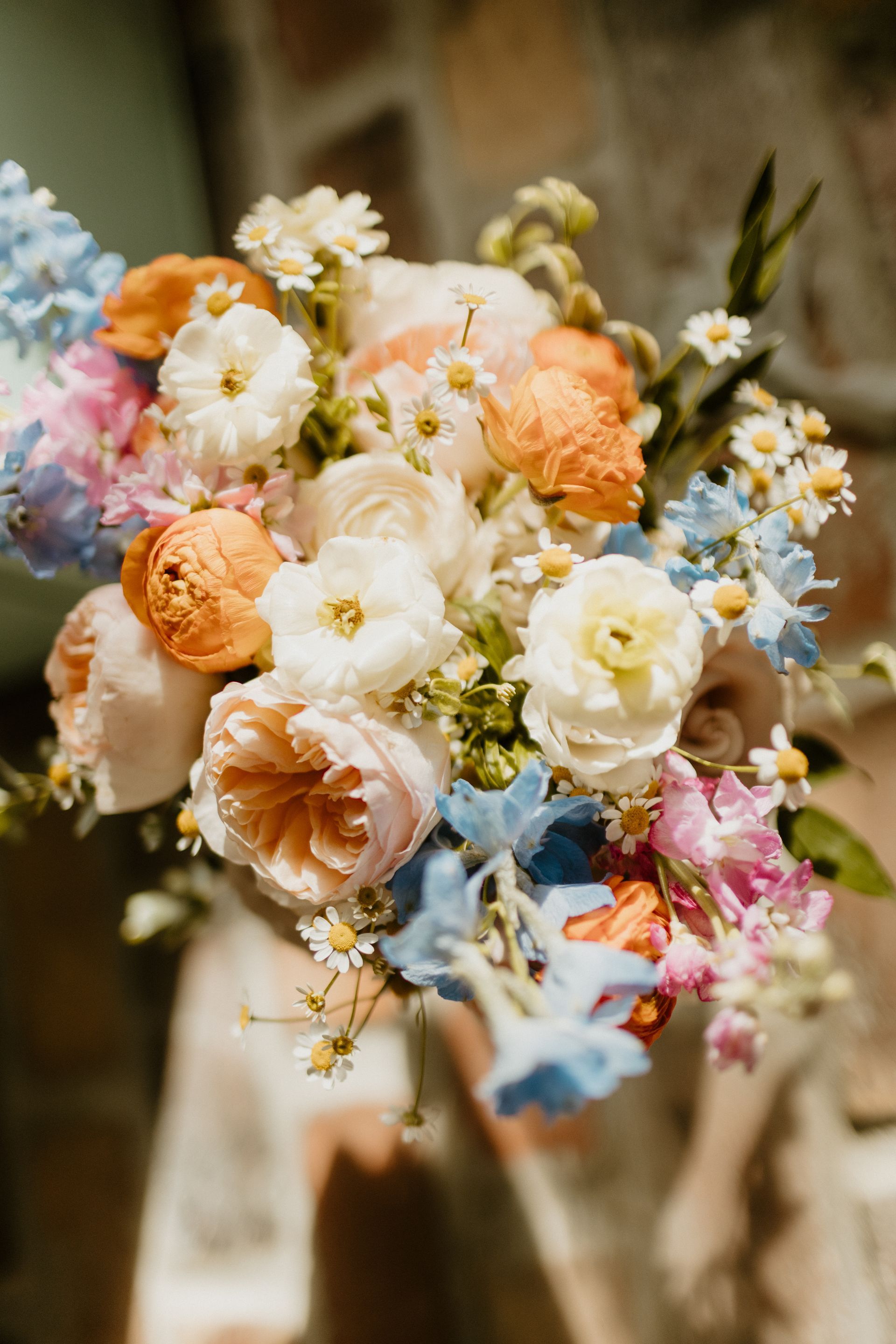 Colorful floral bouquet with orange, pink, white, and blue blossoms, held by someone.
