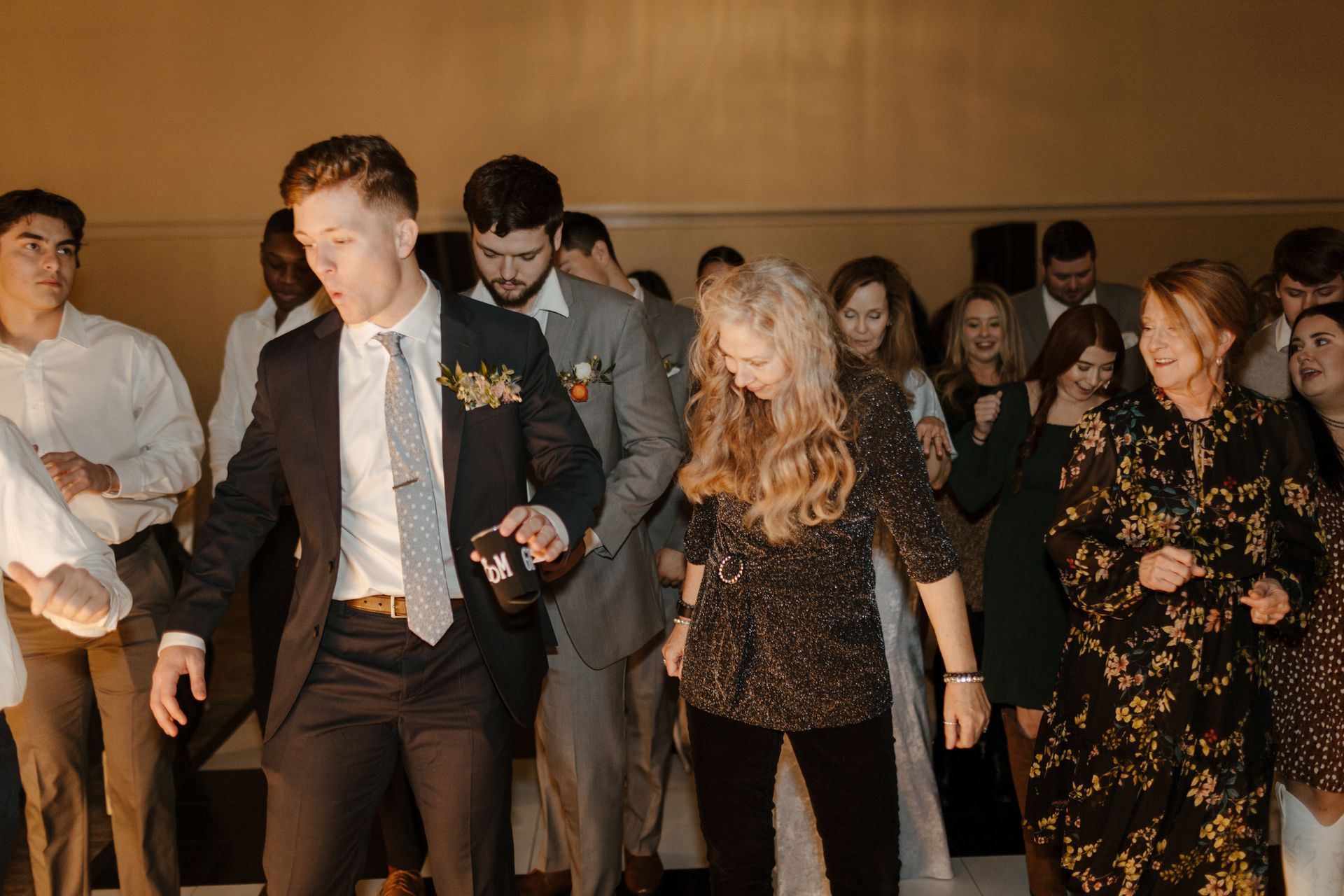People dancing at a party; a man in a suit and woman in a sparkly shirt are in the foreground. Warm, indoor setting.