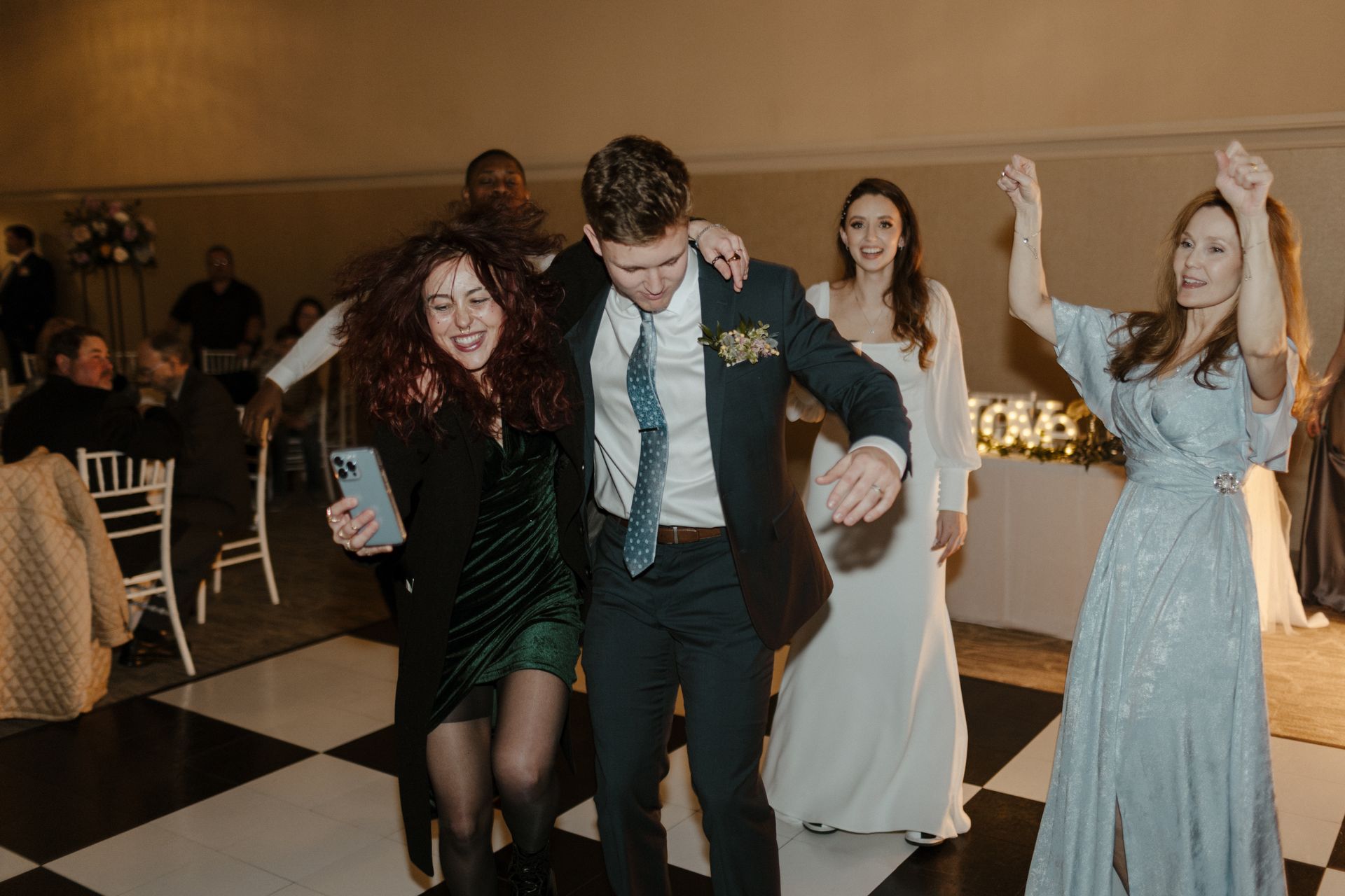 People dancing joyfully at a wedding reception on a black and white checkered dance floor.