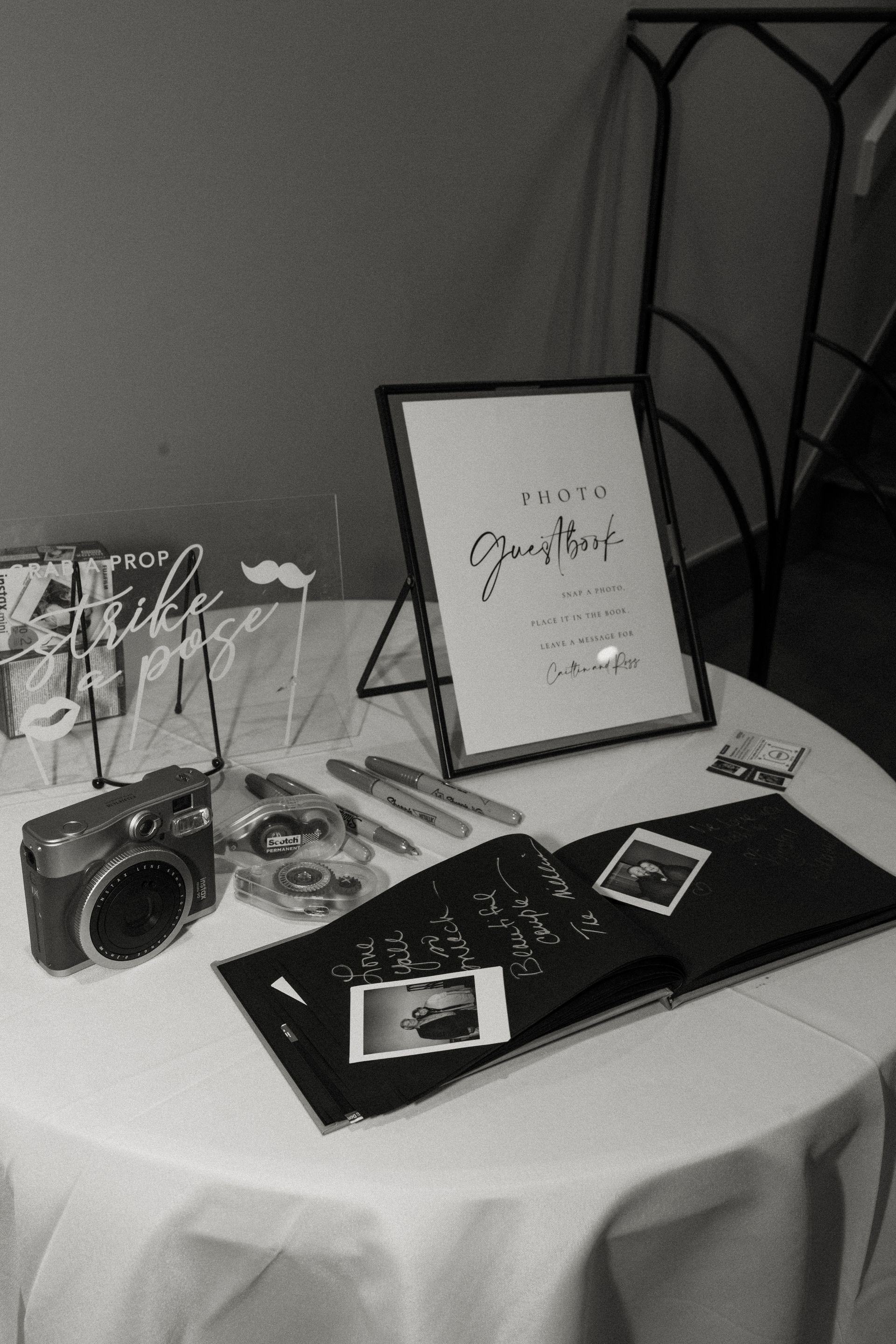 Wedding guestbook table with camera, sign, and photos. Black and white.