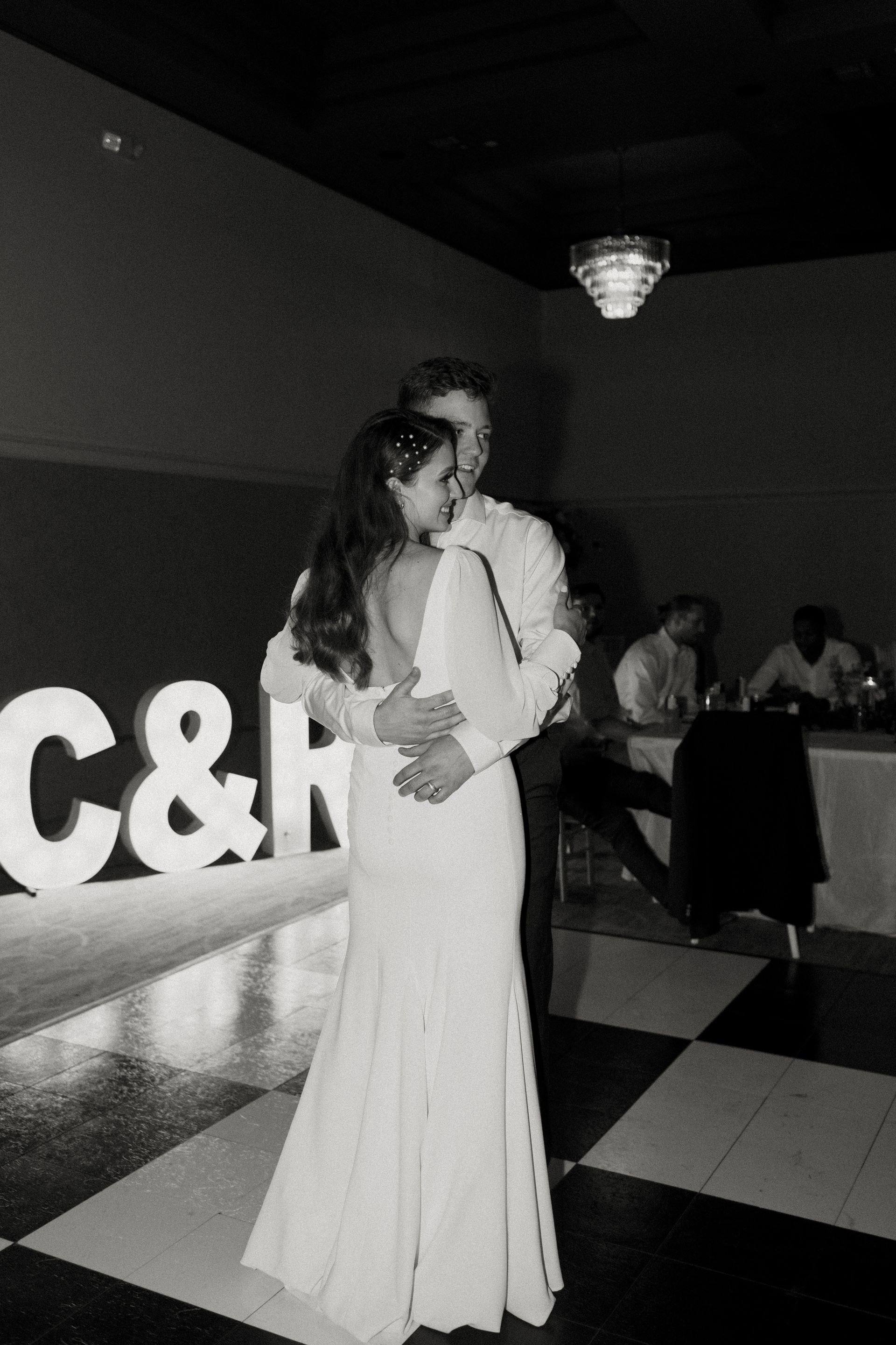 Couple dances on checkered floor at a wedding reception; large lit 