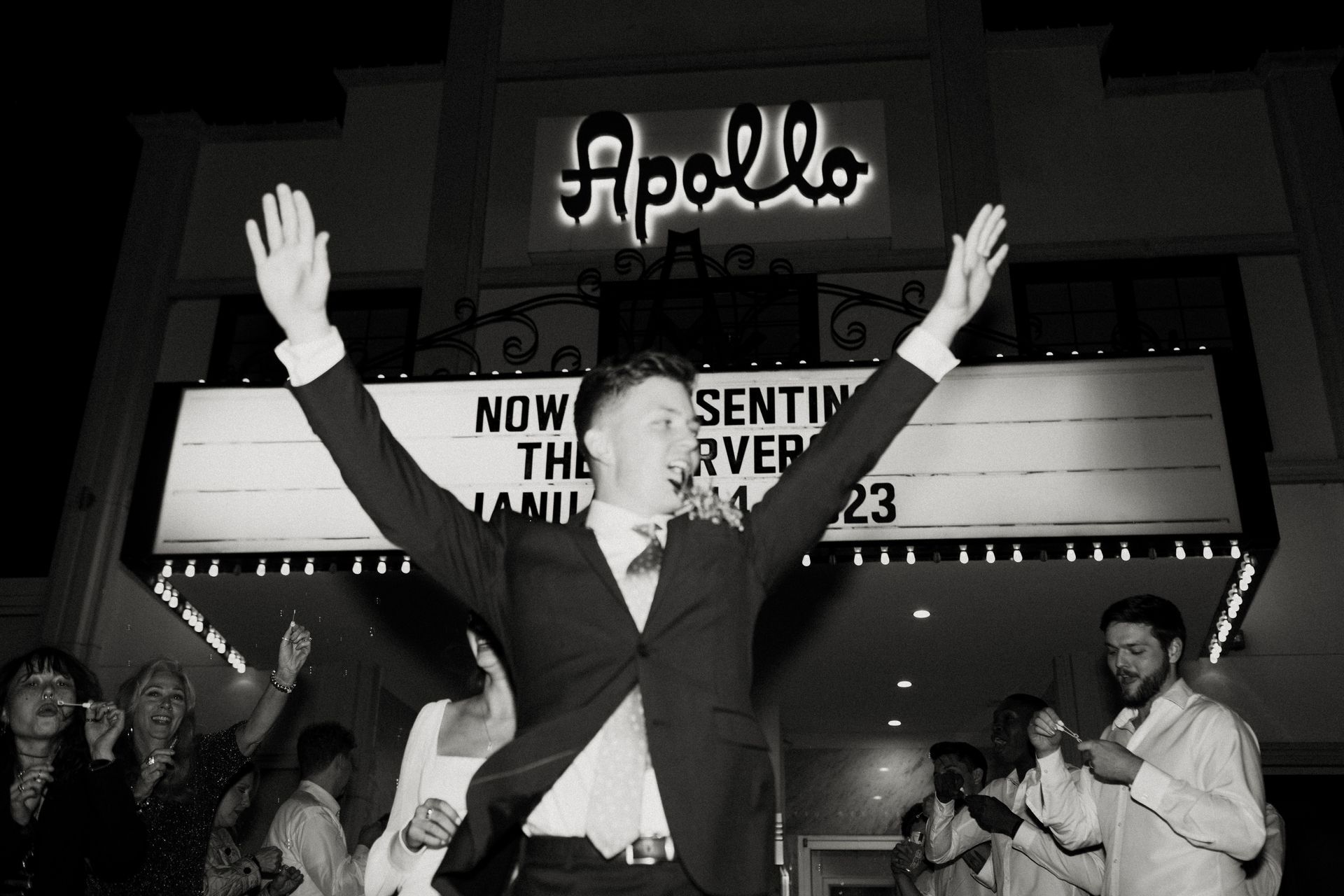 Man with arms raised in front of Apollo Theater, marquee reads 