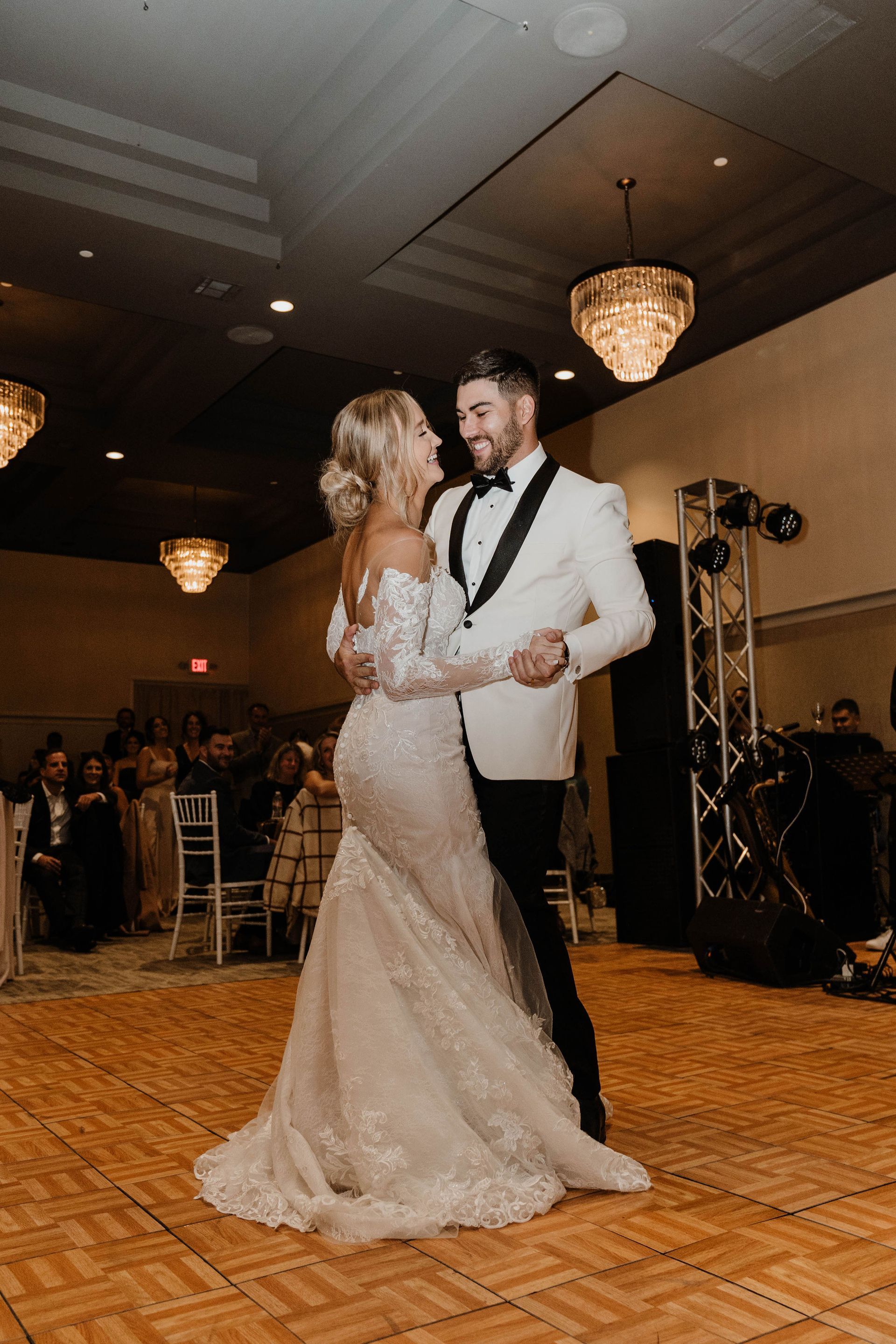 Couple dancing at a wedding reception. Woman in gown, man in tuxedo, smiling, ballroom setting.