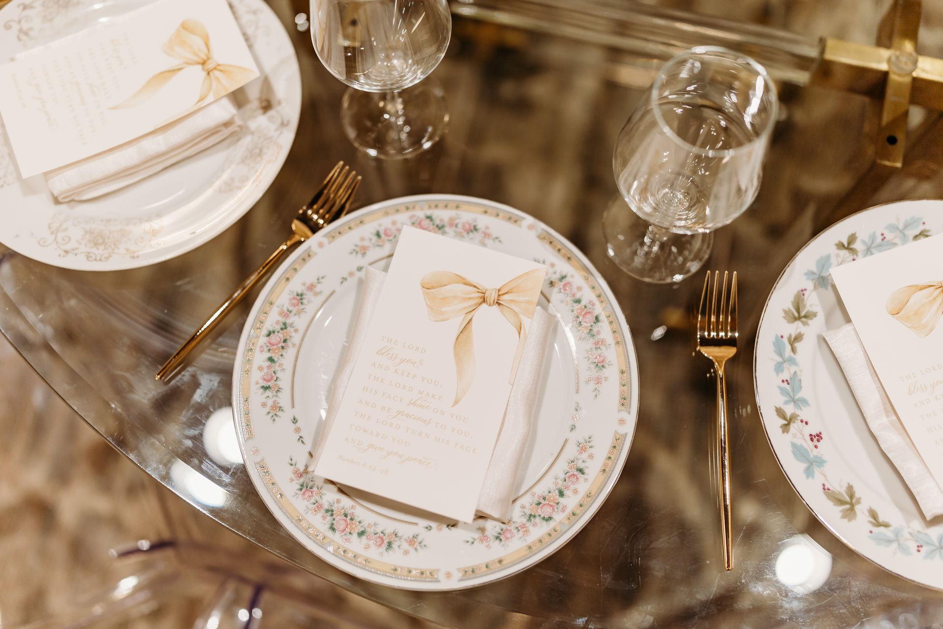 Formal table setting with floral patterned plates, gold forks, and menu cards with bows.