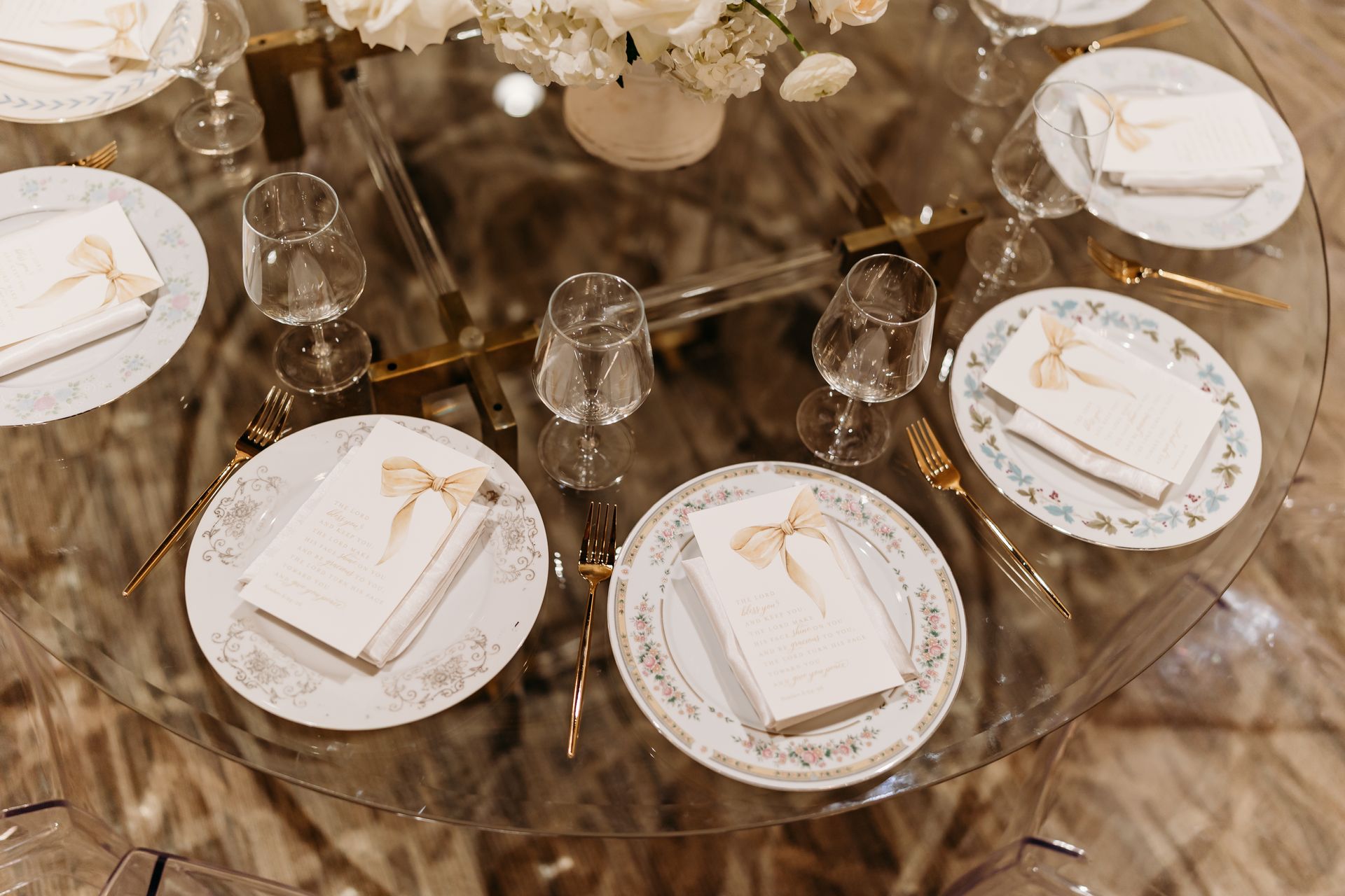 Elegant table setting with plates, silverware, glasses, and floral centerpiece on a glass table.