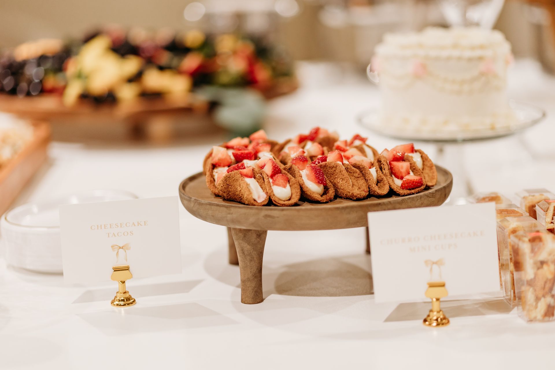 A dessert table with strawberry tarts on a wooden tray, cake, and fruit platter.