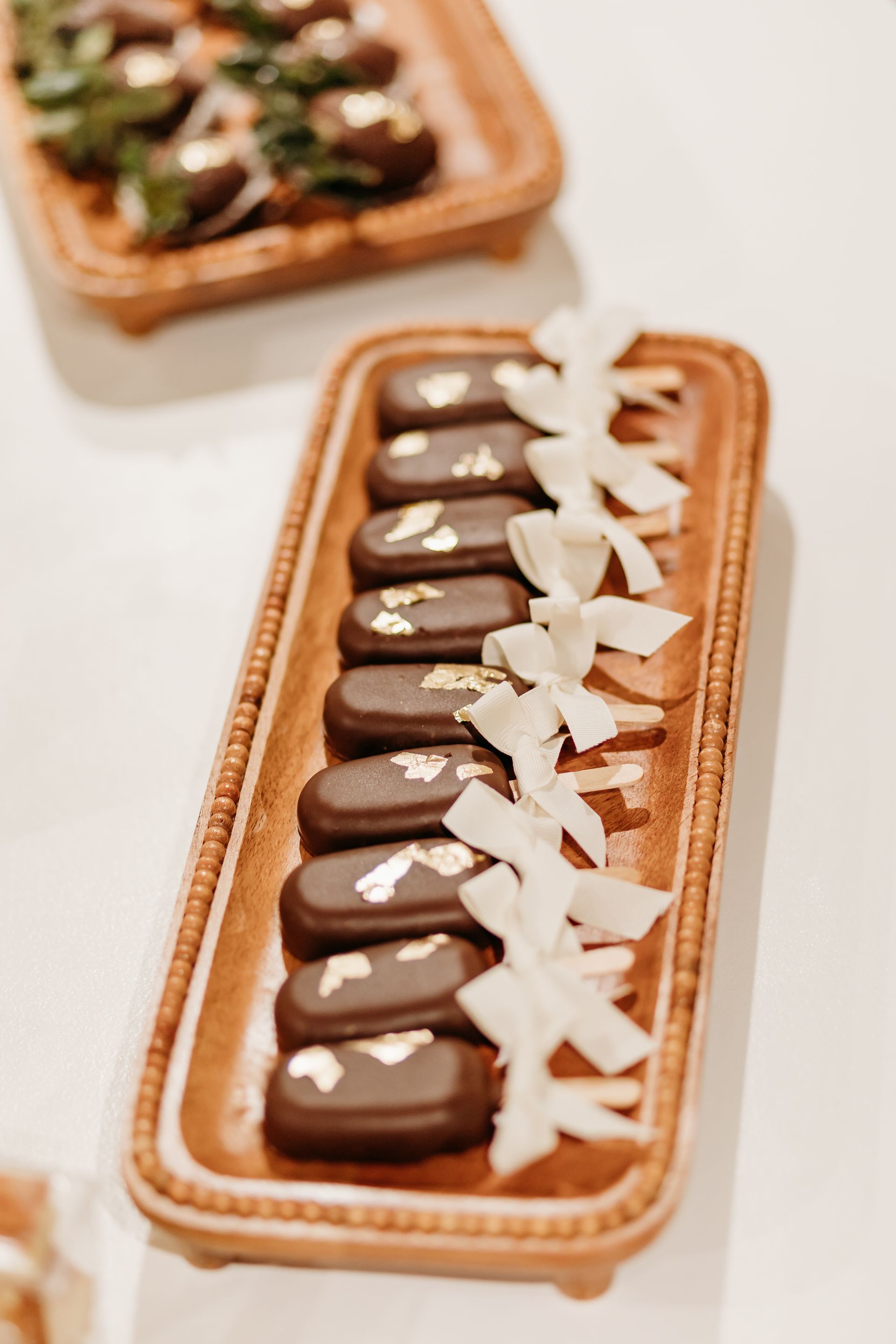 Chocolate desserts with gold leaf on a wooden tray, decorated with white flowers.