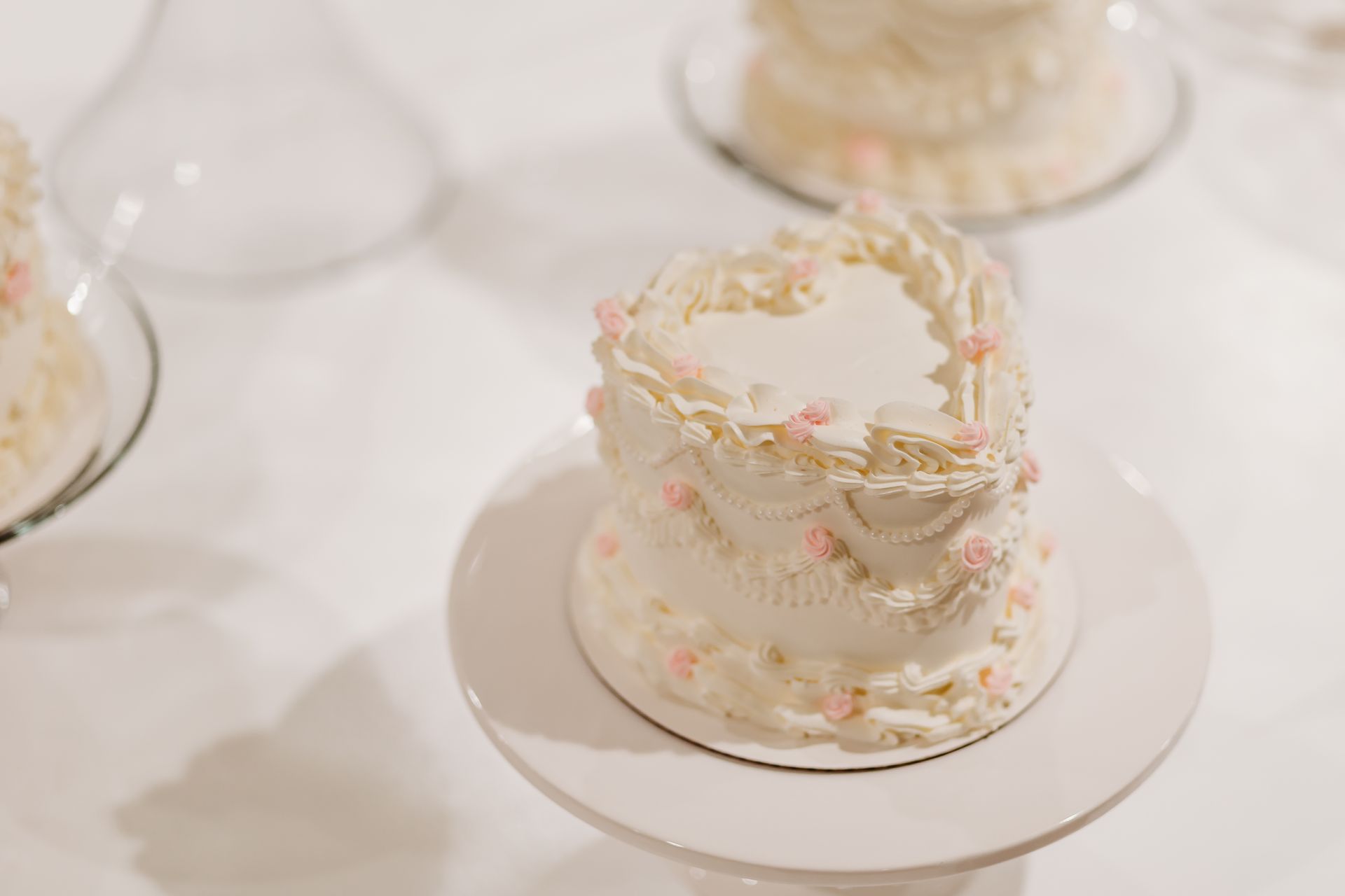 Small white frosted cake decorated with pink flowers, on a white cake stand.