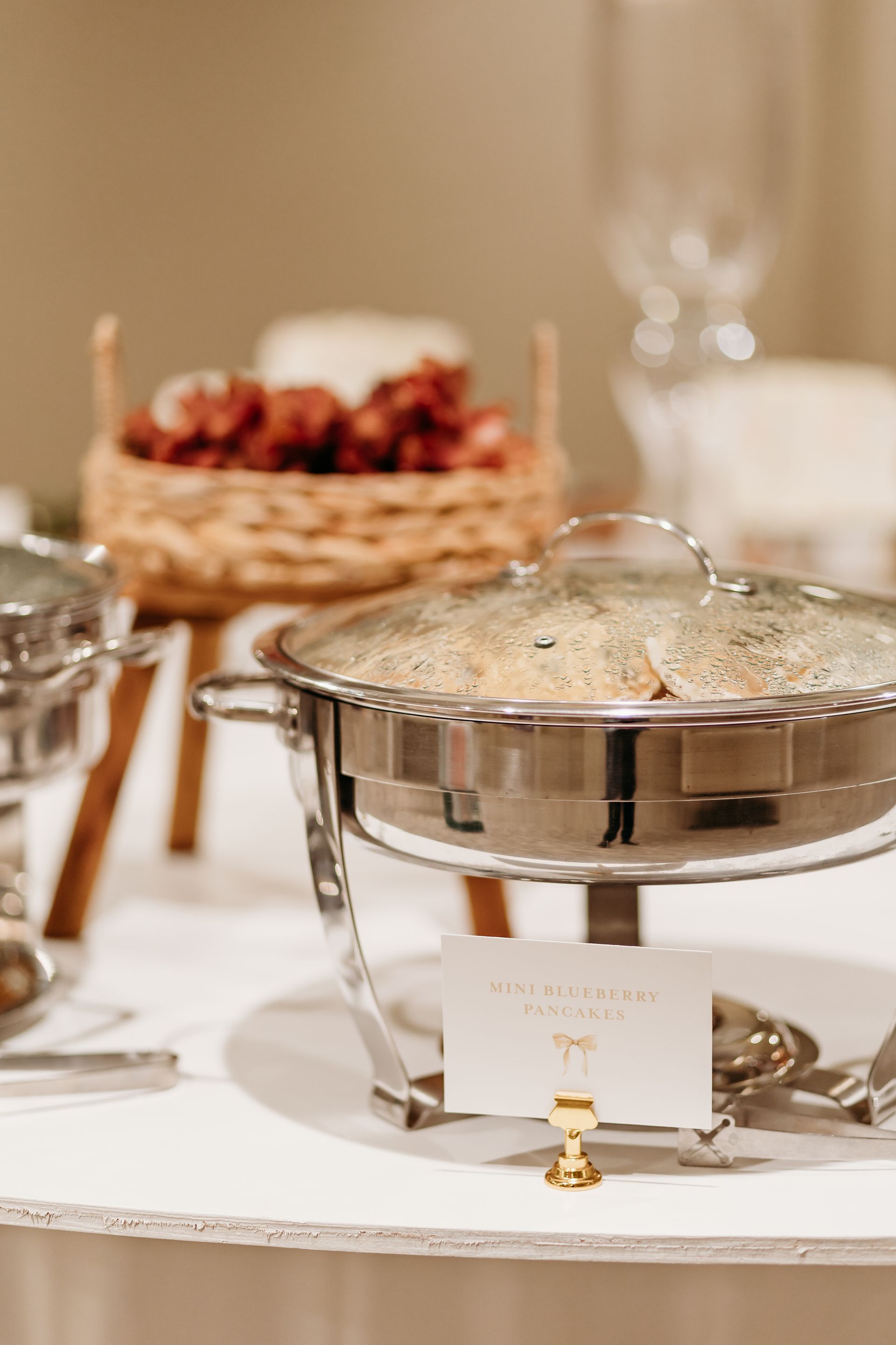 A buffet table with a silver chafing dish, food baskets, and a name card.
