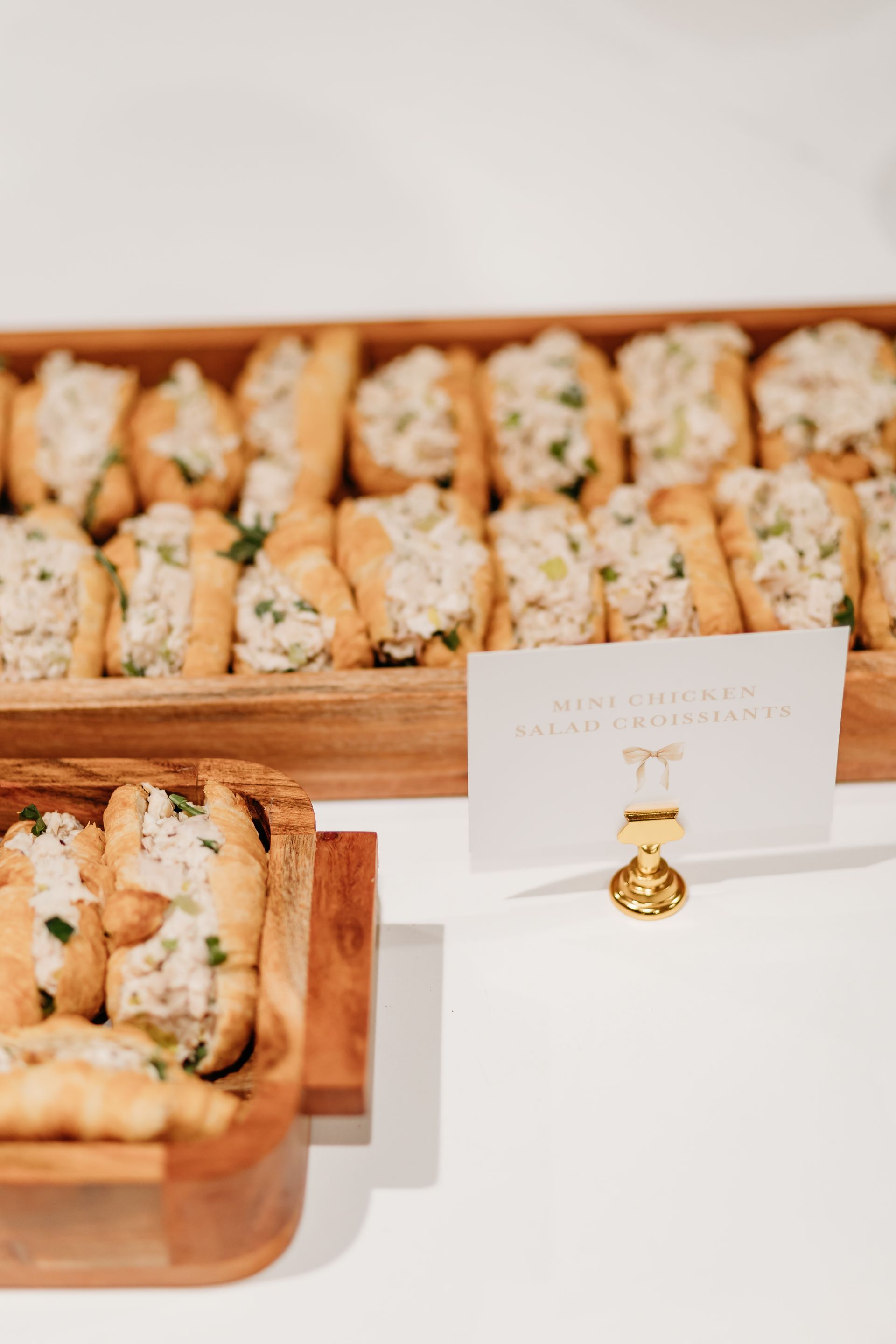 Wooden trays of chicken salad croissant bites with a gold card holder.
