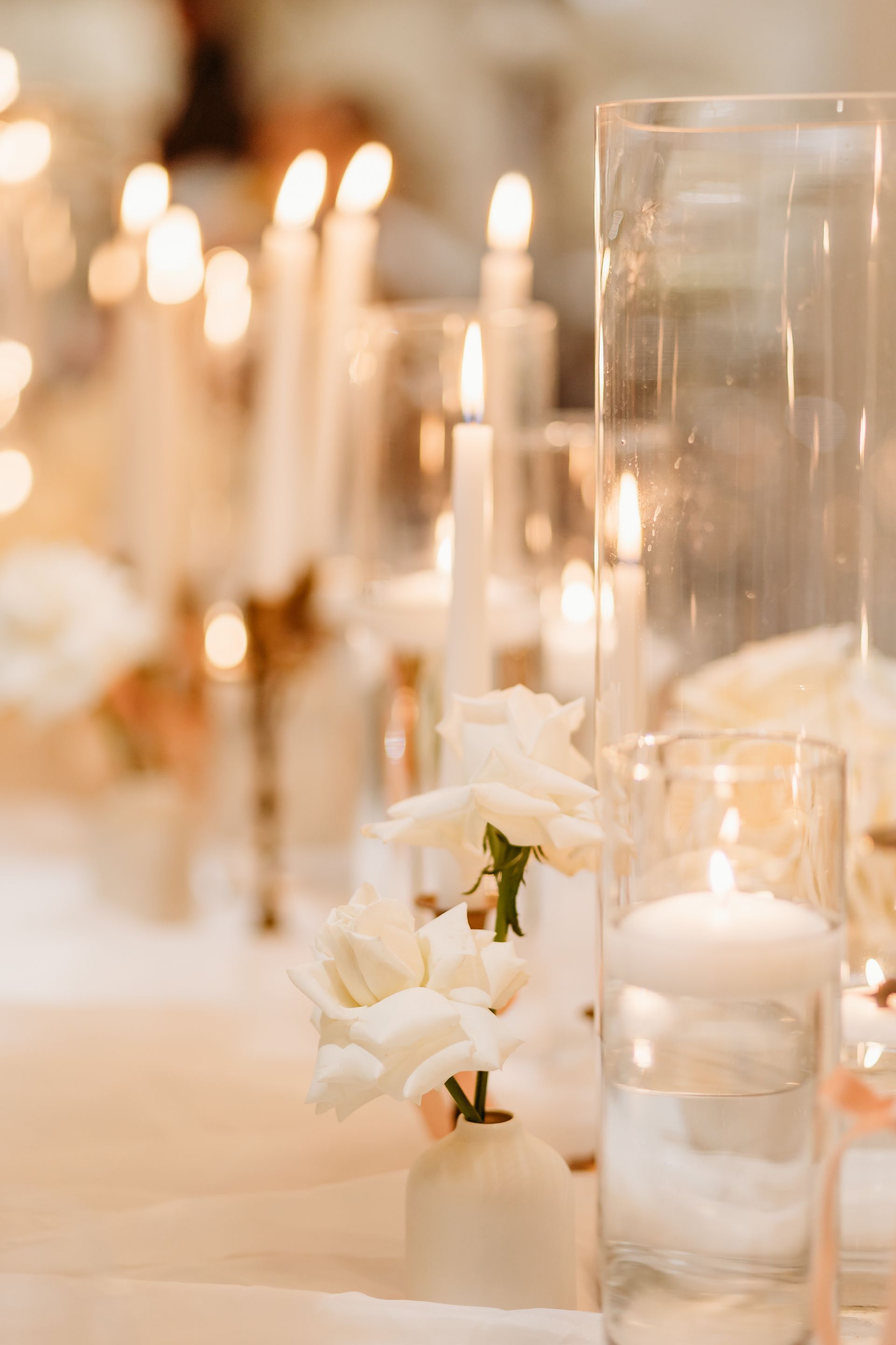 Elegant wedding table centerpiece with white roses, candles, and glass vases.