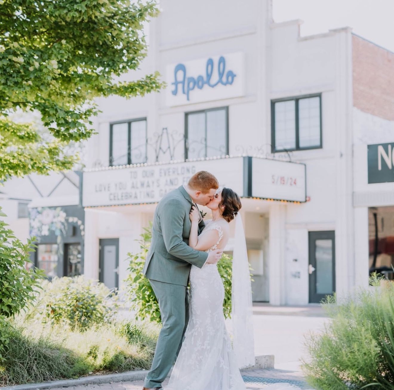Couple kissing in front of the Apollo Theater. Bride in white dress, groom in grey suit, sunny day.