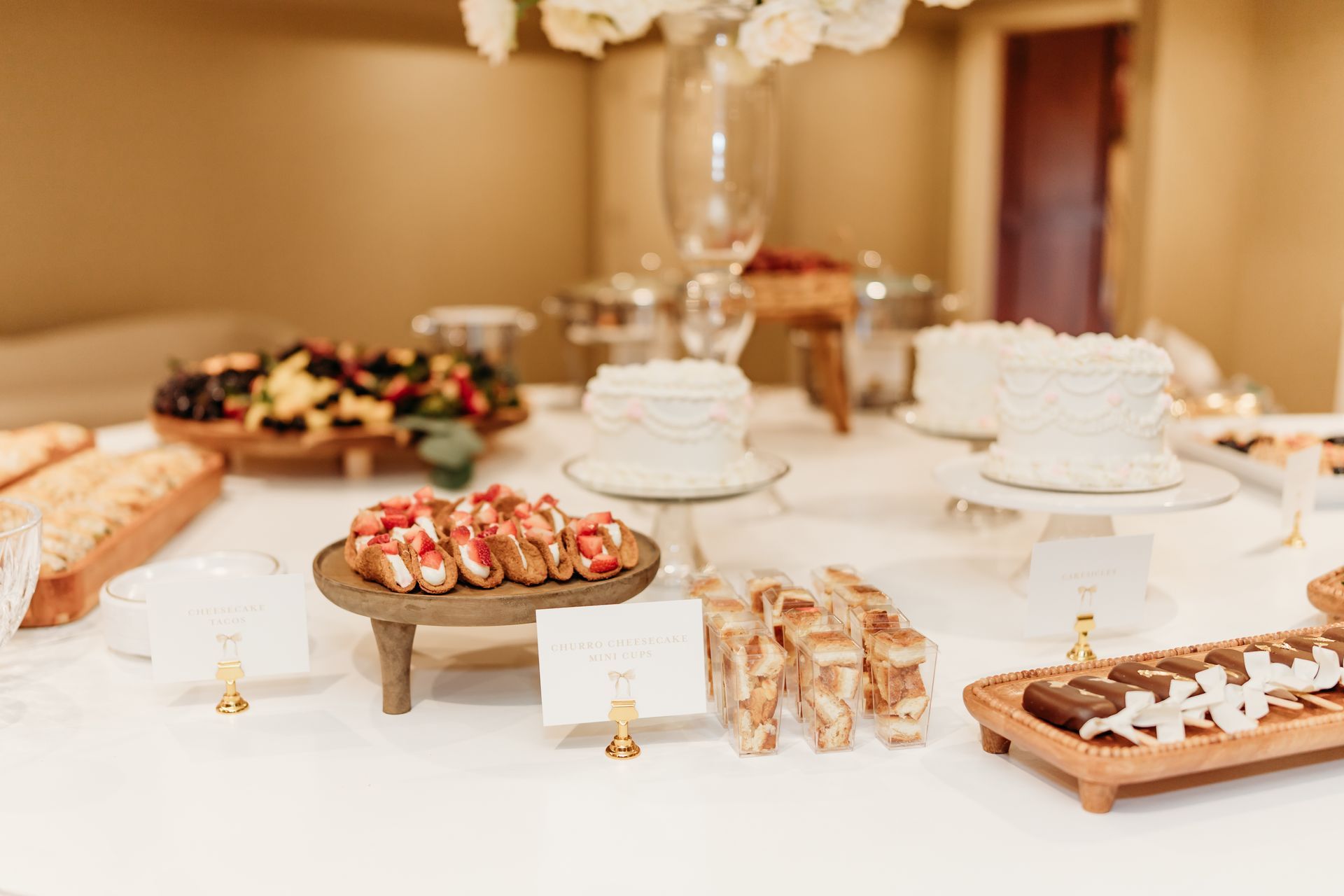 A buffet table with various desserts, including cakes and appetizers, set against a neutral background.
