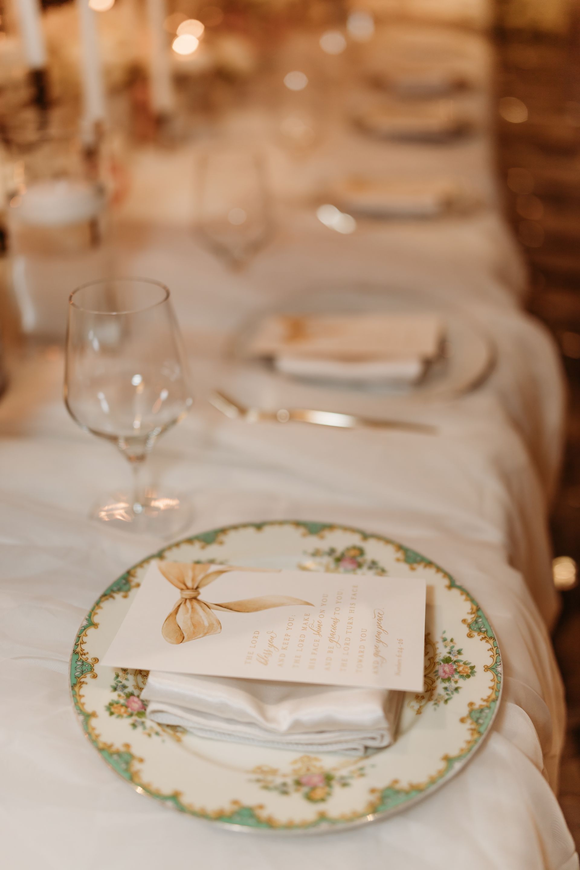 Elegant table setting with floral plate, glass, folded napkin, and menu card on white tablecloth.