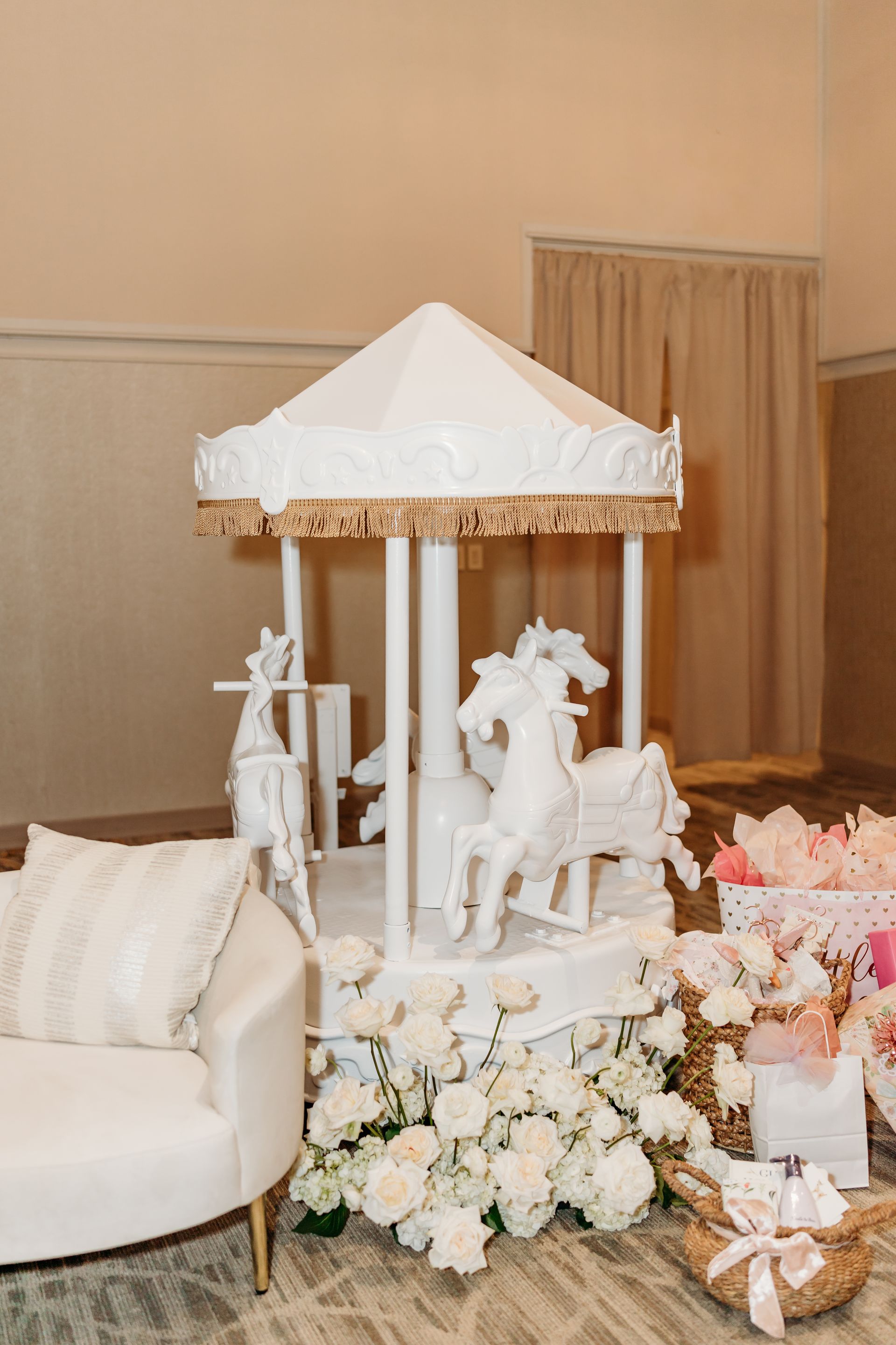 White carousel decorated with flowers; sofa and gift basket nearby.