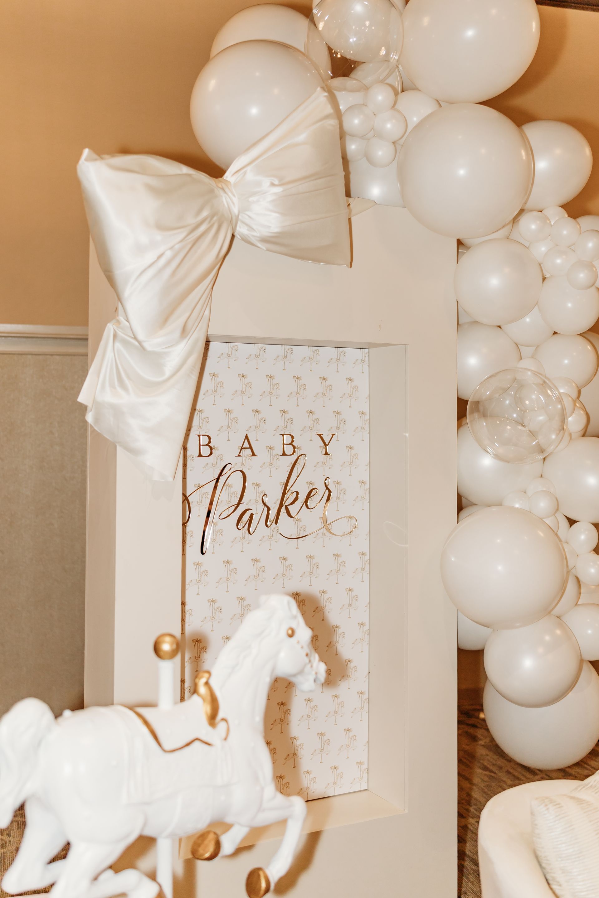 Baby Parker sign with white balloons, bow, and carousel horse decor.