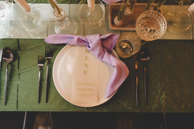 Elegant table setting with white plate, lavender napkin, and menu on a green surface.