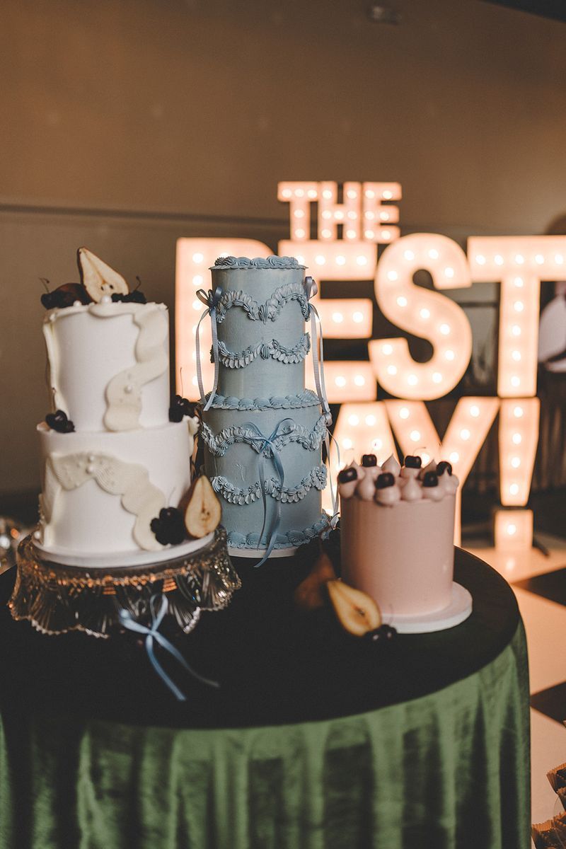 Three tiered cakes on a green table with a lighted sign that says 