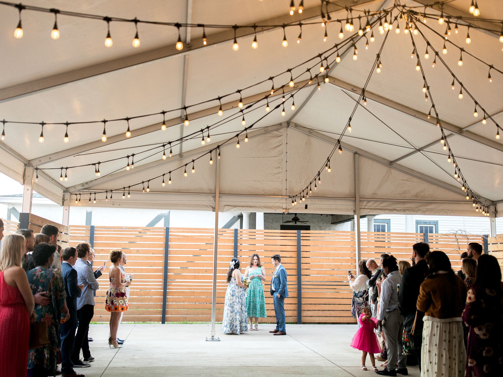 Wedding ceremony under a tent with string lights; couple and guests in attendance.