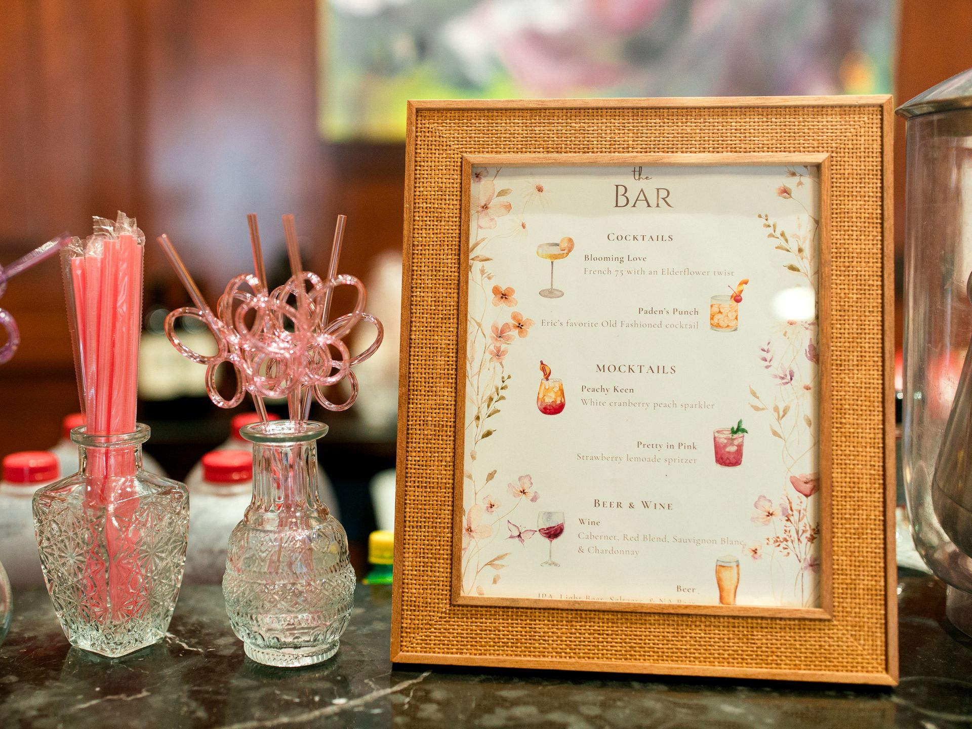 Bar menu in a gold-framed sign next to drink stirrers in ornate glass vases.