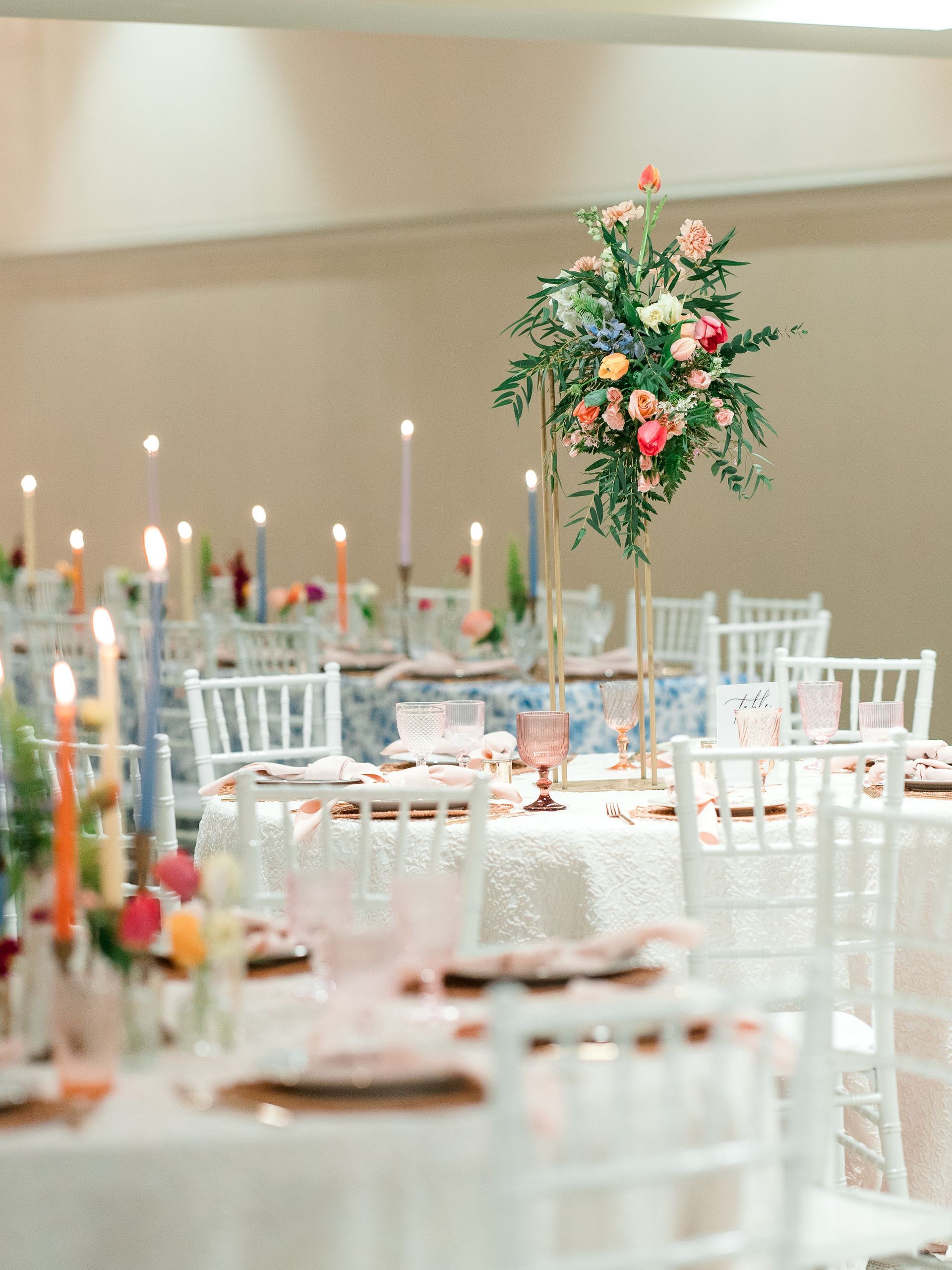 Elegant wedding reception with round tables, floral centerpieces, candles, and white chairs.