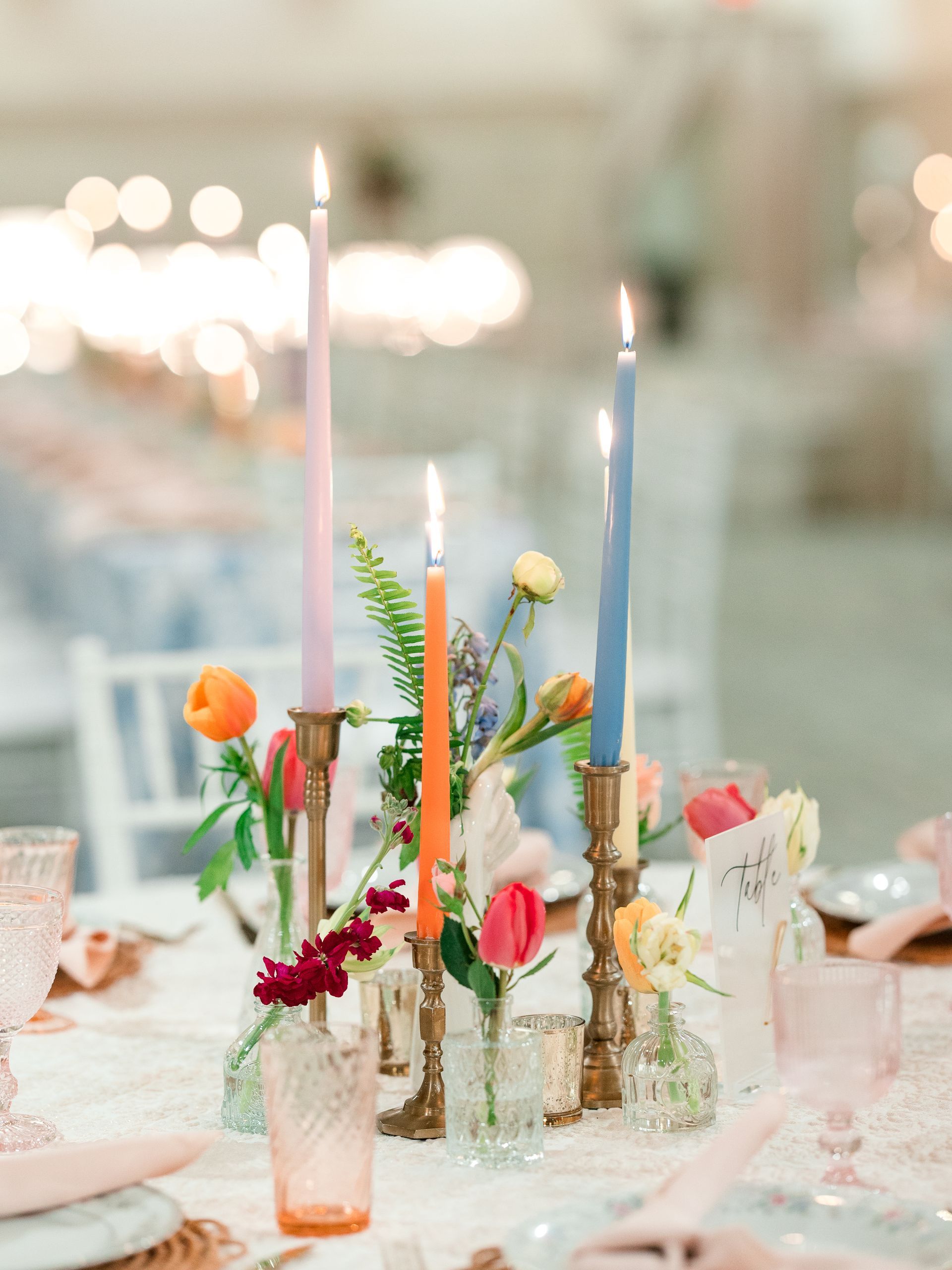 Centerpiece with lit colorful candles and flowers on a table, soft lighting.