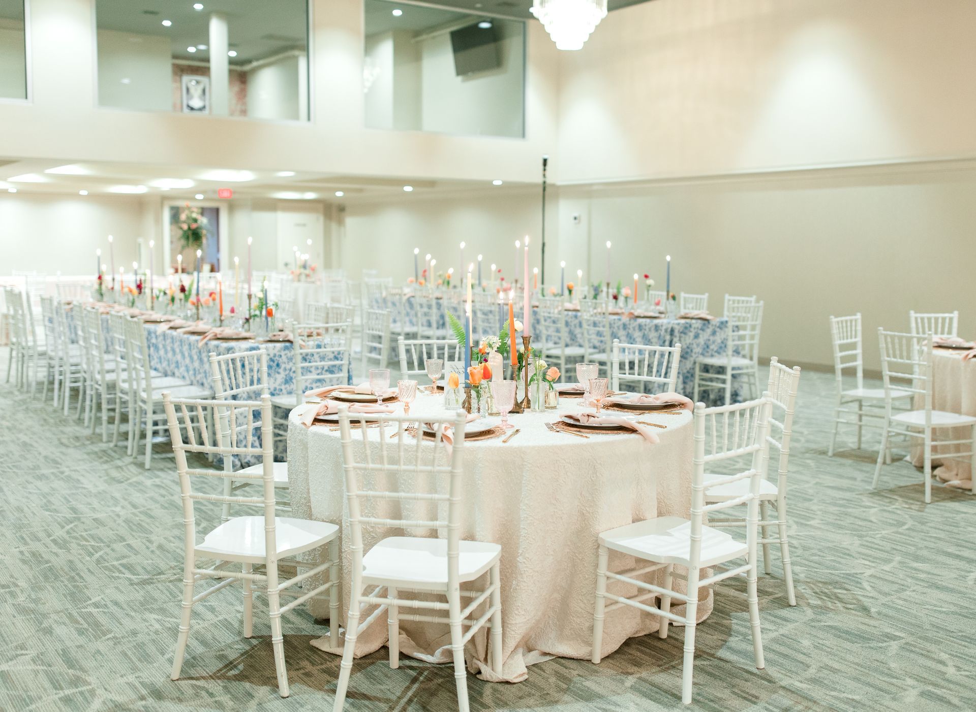 Banquet hall set with white chairs, round and rectangular tables, floral centerpieces.