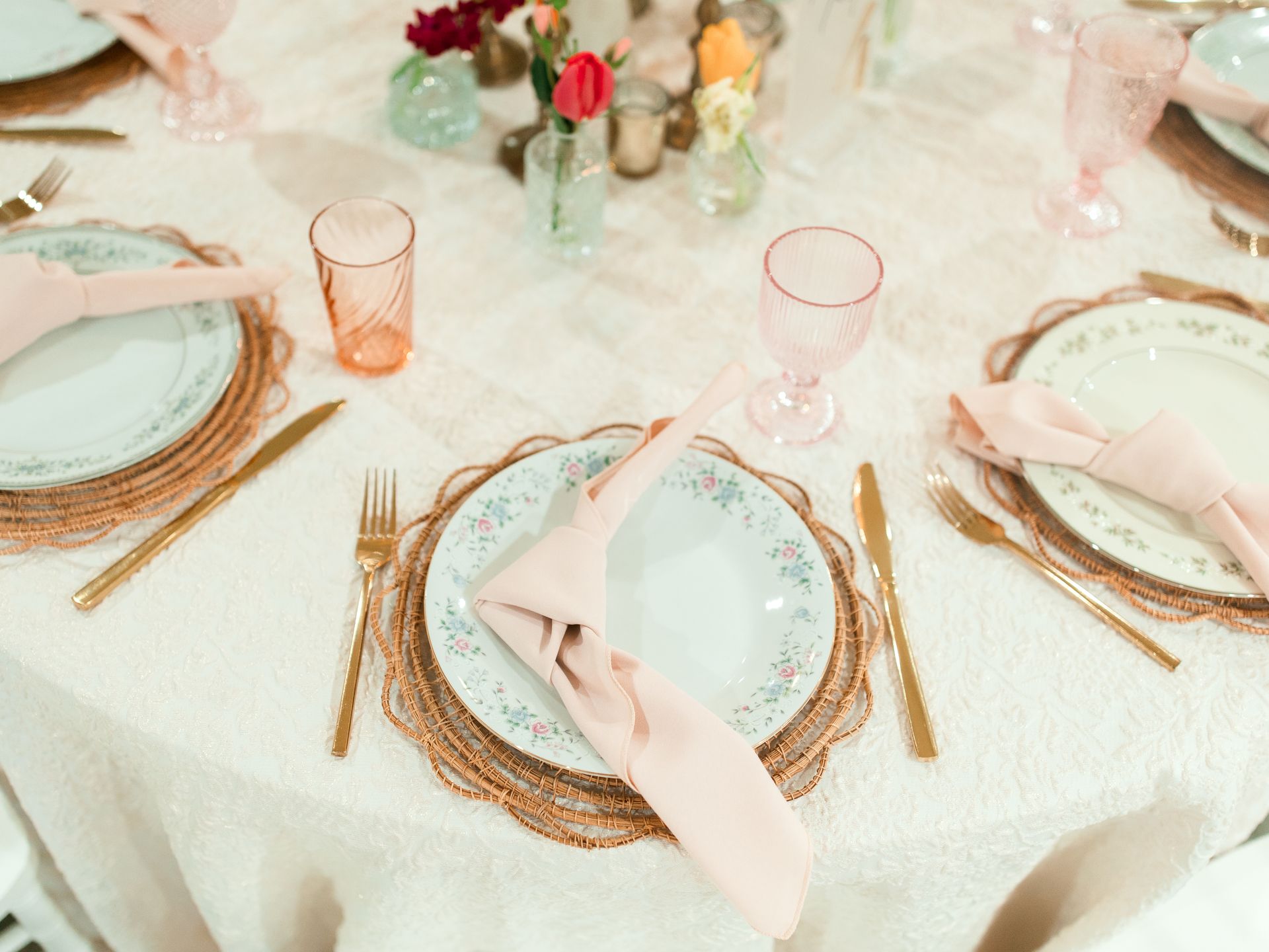Formal table setting with pink and gold accents, featuring place settings and centerpieces.