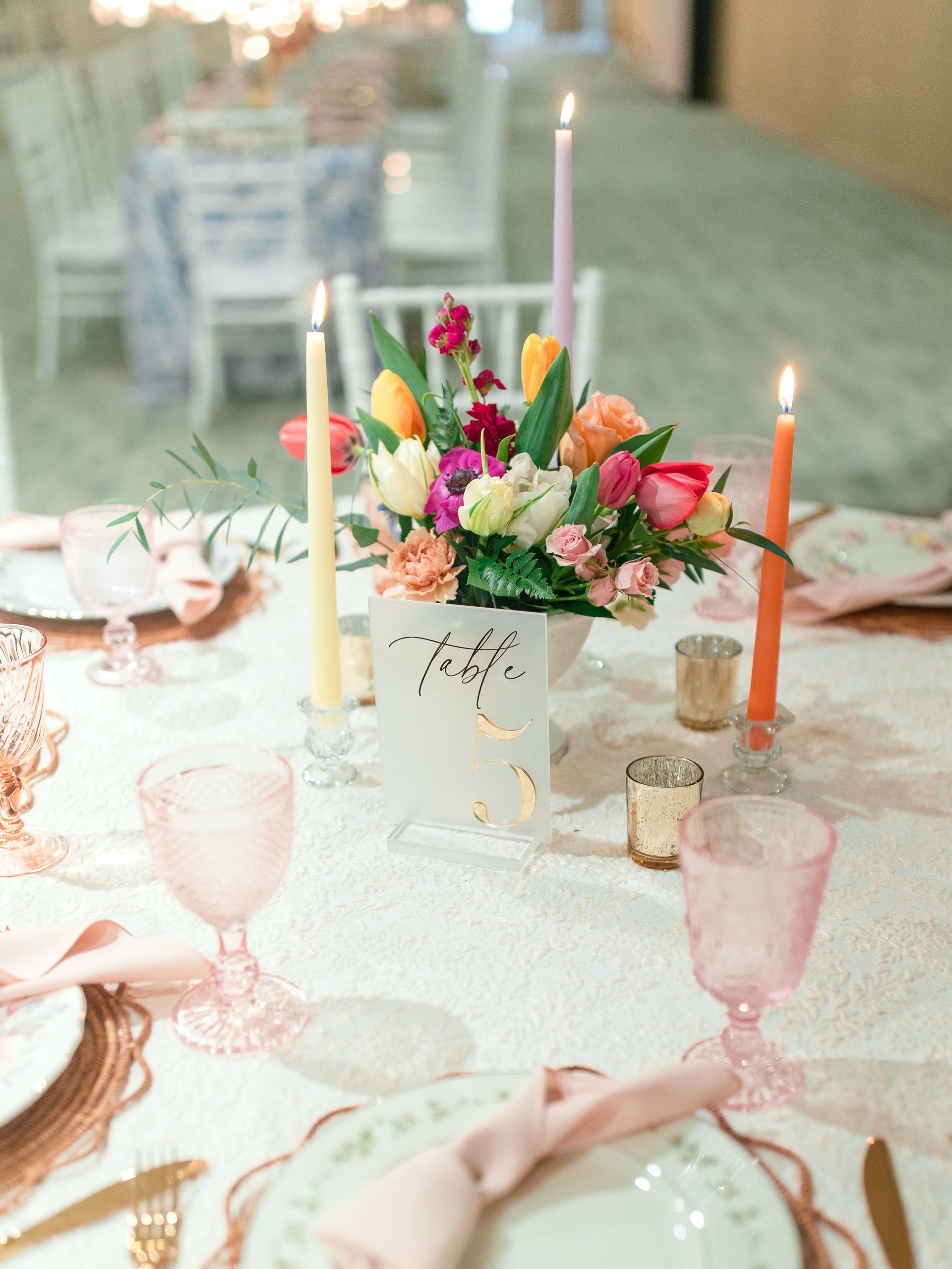 Elegant table setting with a floral centerpiece, candles, and pink glassware.