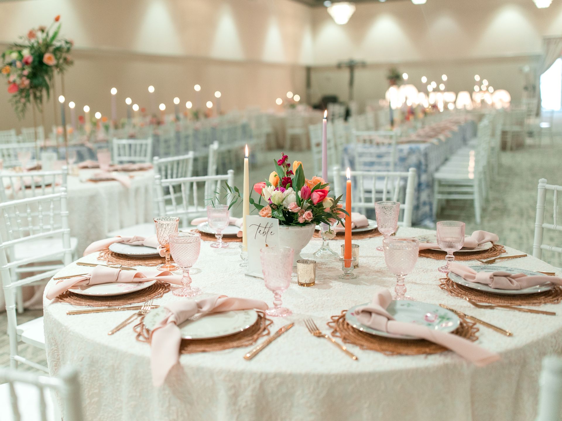Elegant wedding reception with round tables set for guests. Pink and gold accents.