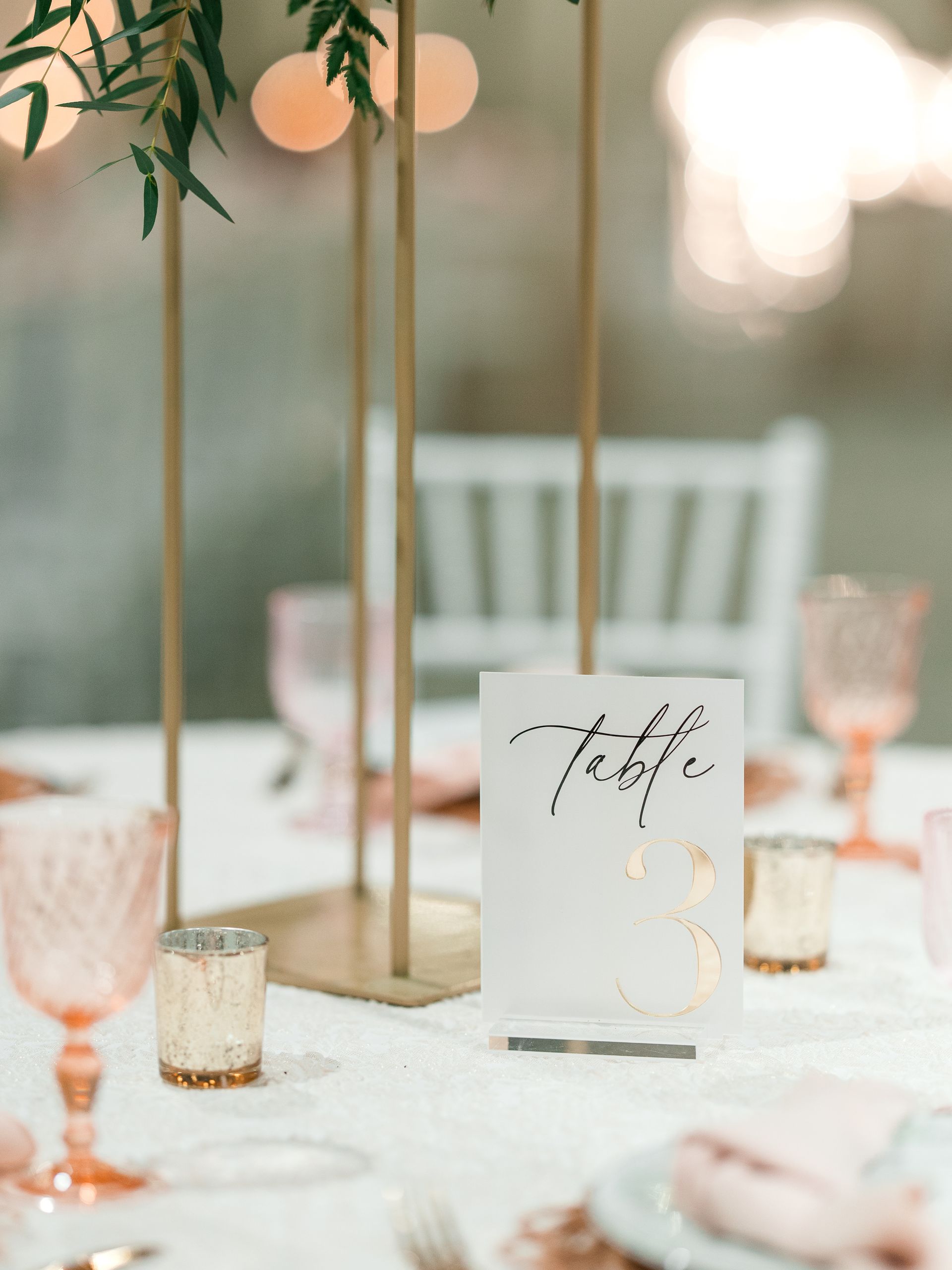 Elegant table setting with gold accents, floral centerpiece, and table number card.