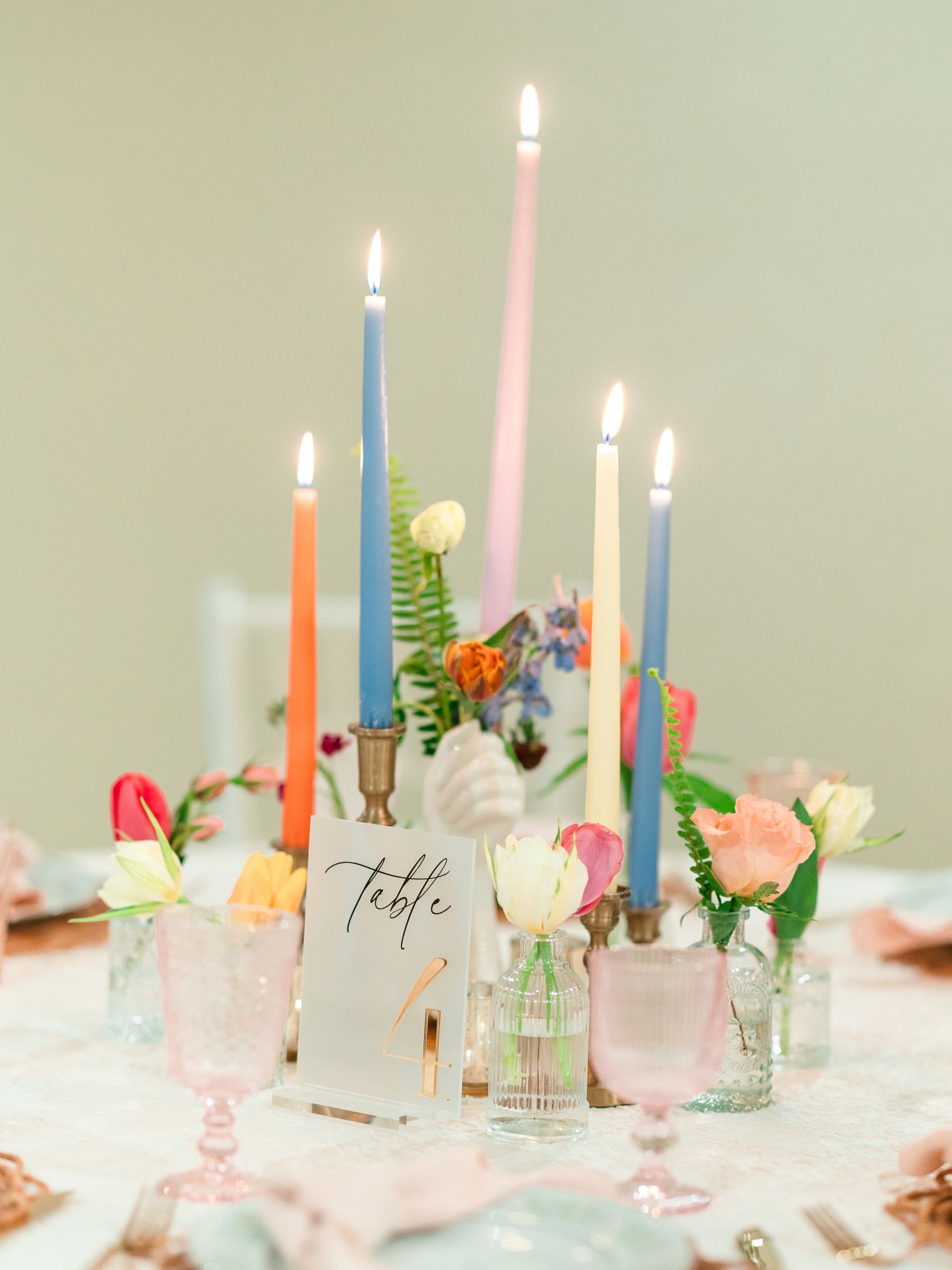 Colorful candles and flowers on a table setting, with pink and blue glassware.
