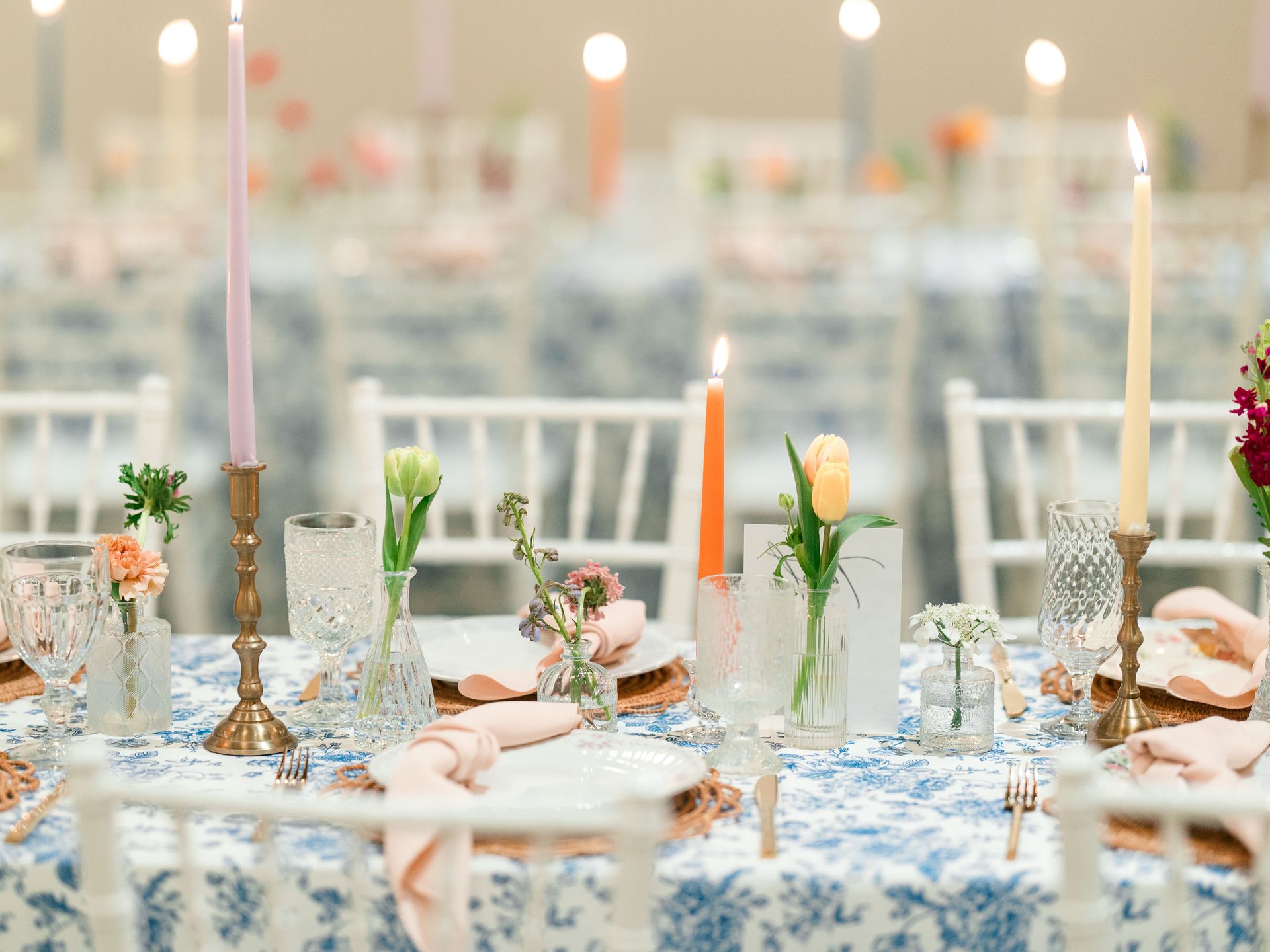 Table setting with blue floral tablecloth, pastel candles, and fresh flowers.