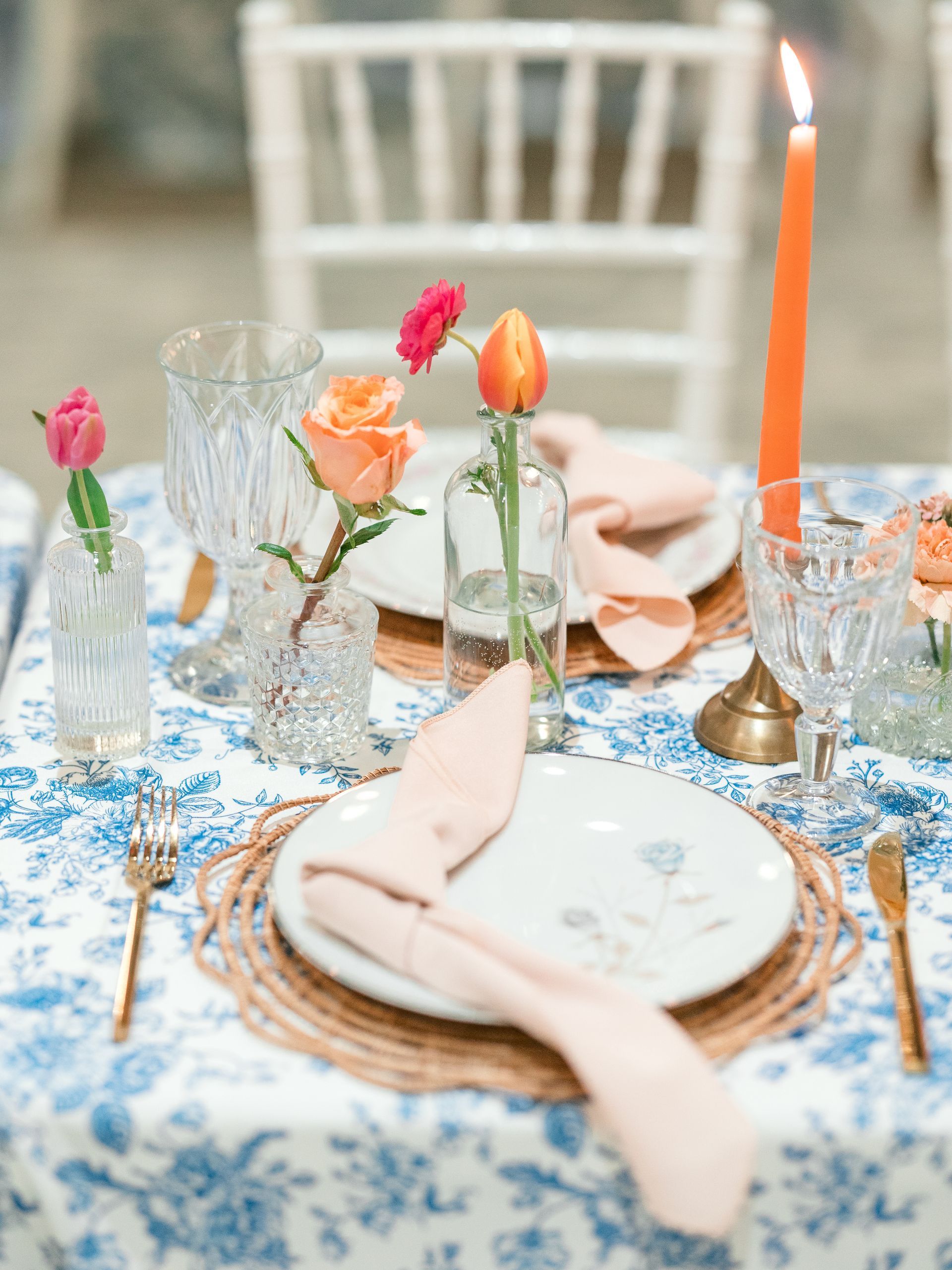 Elegant table setting with floral tablecloth, flowers, glassware, and peach-colored napkins.