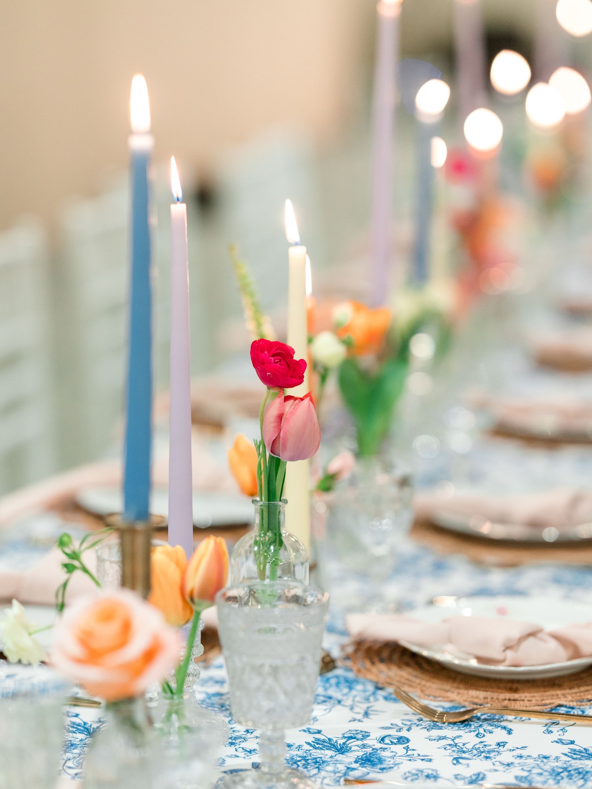 Floral centerpiece with pastel candles, set on a table with blue and white floral tablecloth.